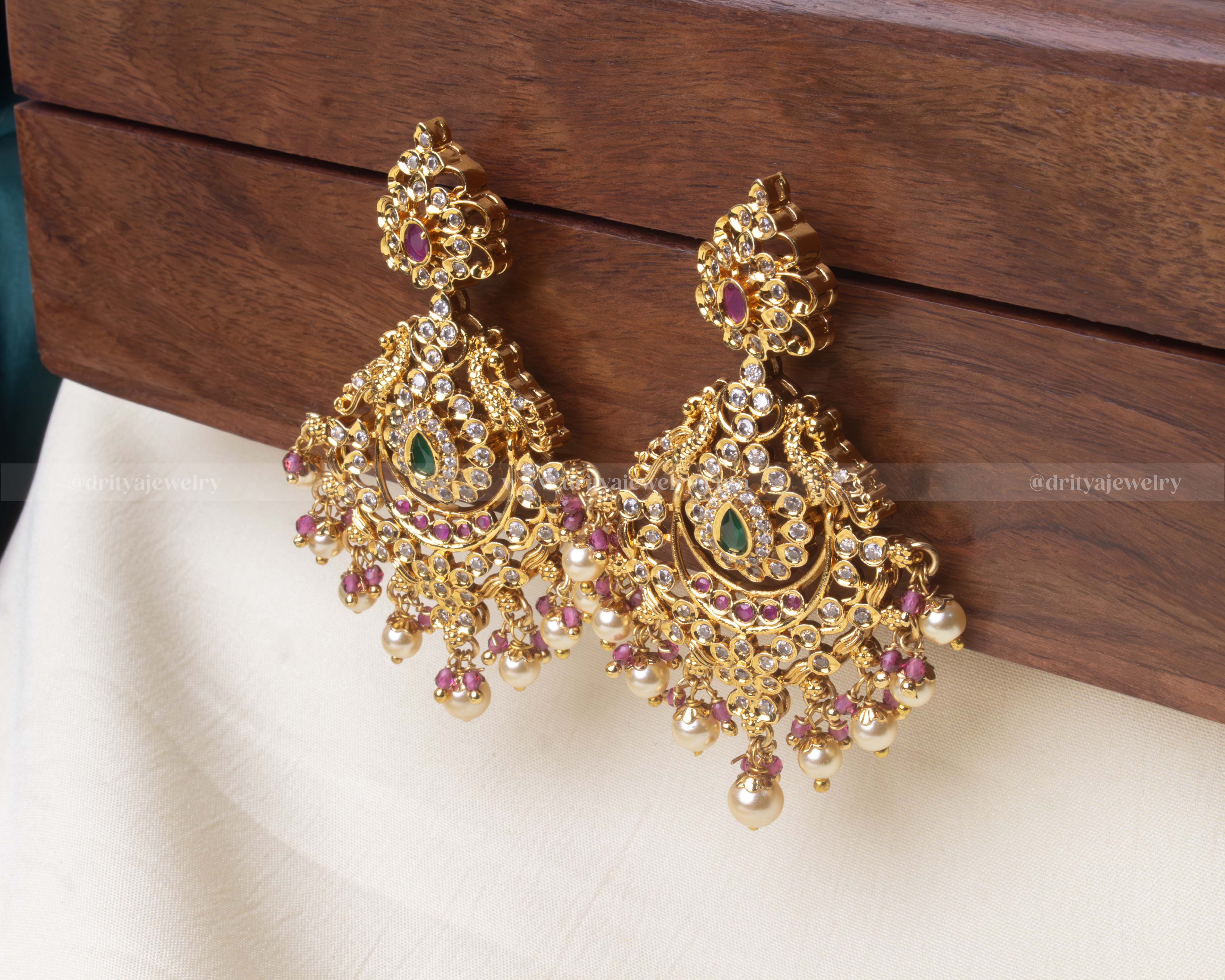 Elegant premium dangler earrings featuring green and ruby accents, cubic zirconia detailing, and hanging pearl embellishments.