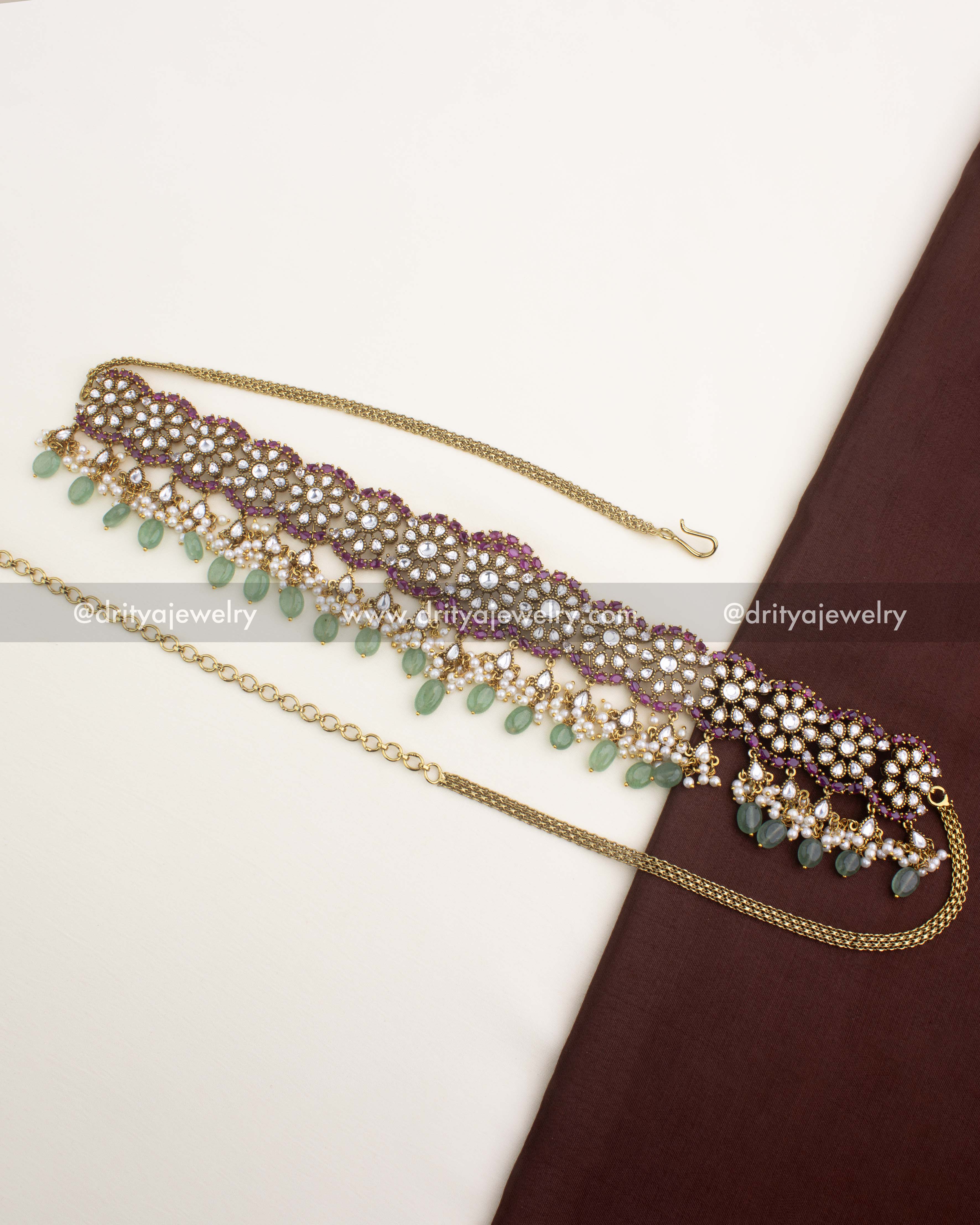 Antique gold Polki Kundan hip chain with floral motifs, ruby accents, and green bead drops from Dritya Jewelry.