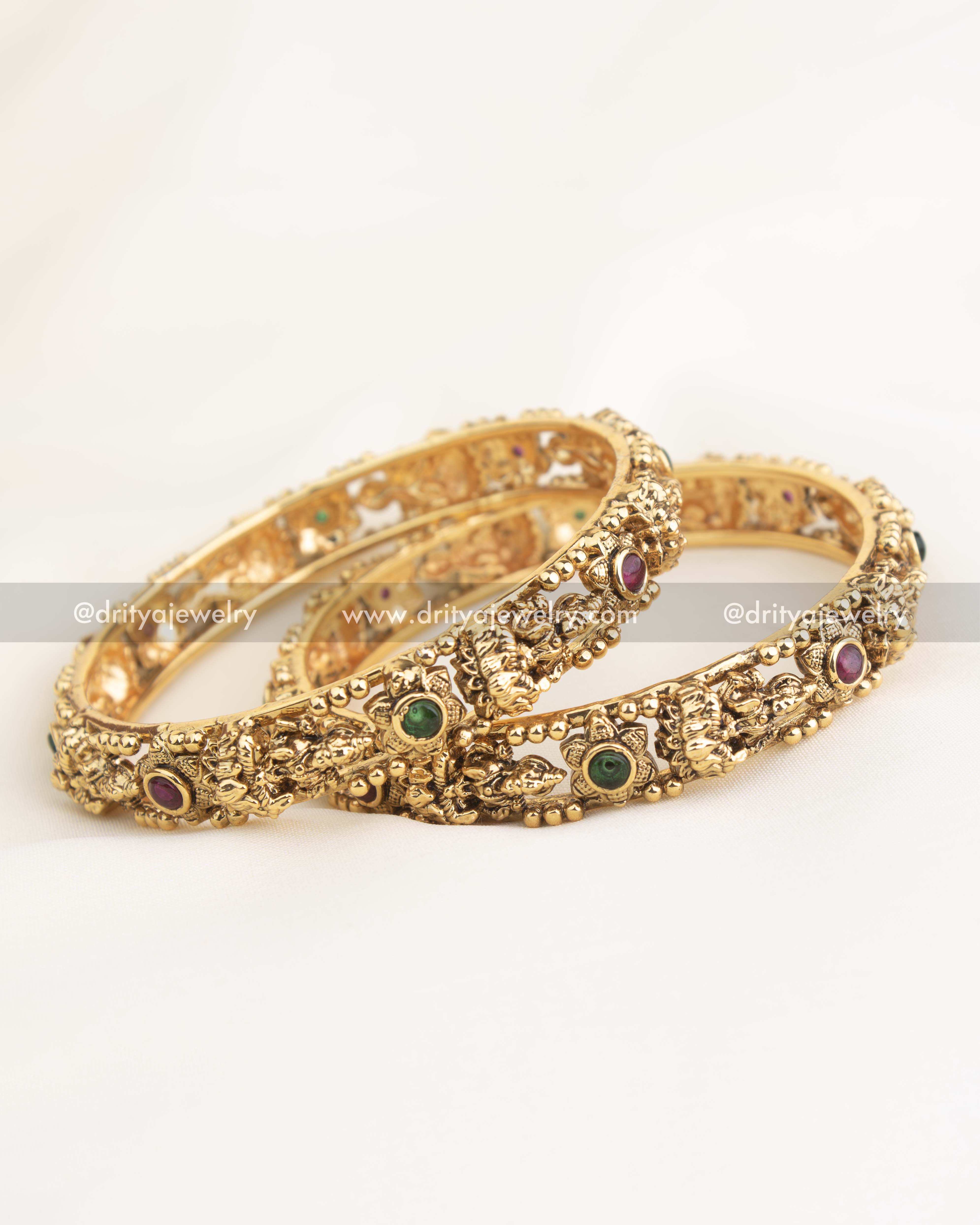 Handcrafted temple bangles featuring goddess motifs, ruby and emerald accents, and antique gold polish by Dritya Jewelry.