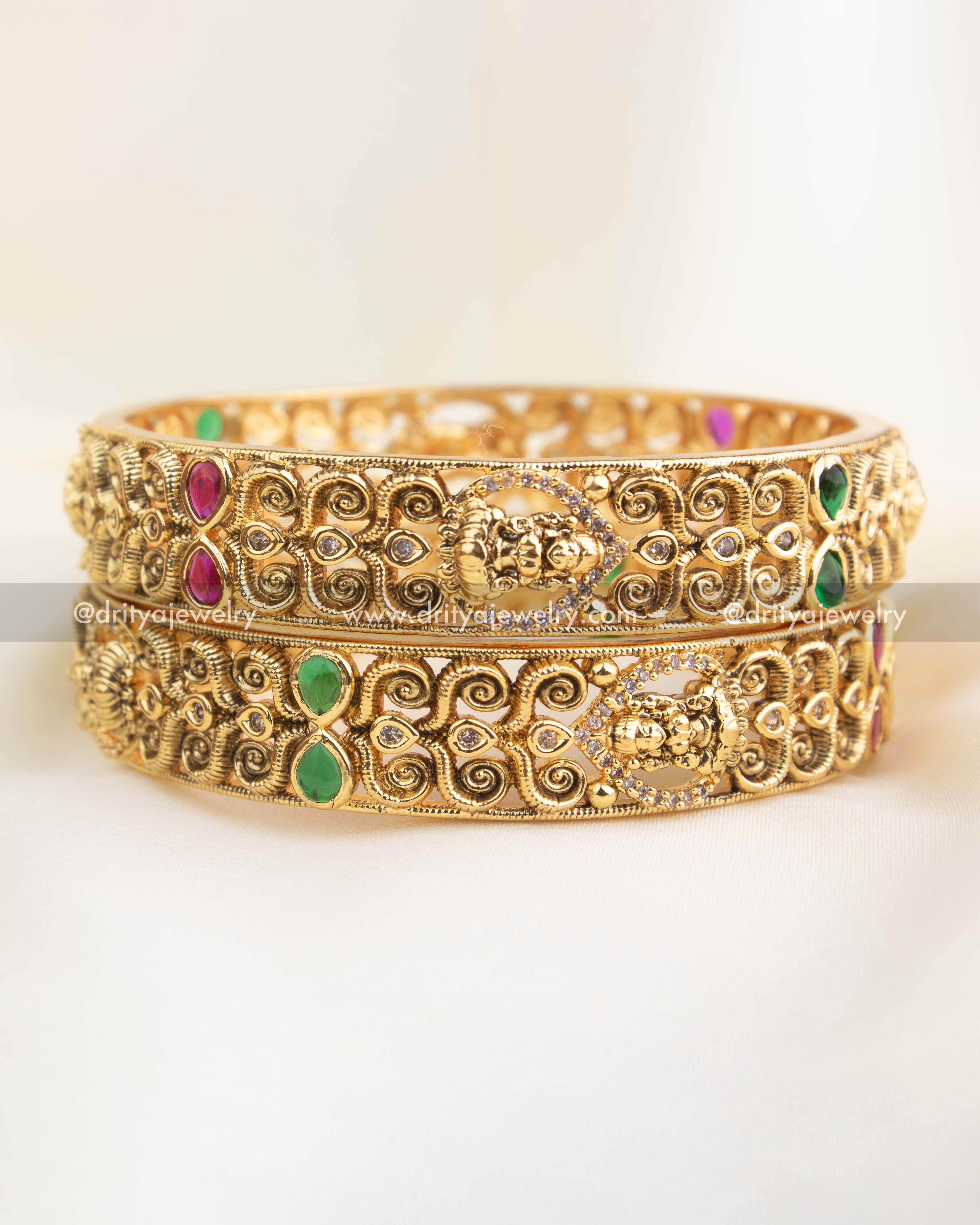 Antique temple bangle with Nakshi goddess motif, ruby and emerald stone highlights, and intricate scrollwork design.