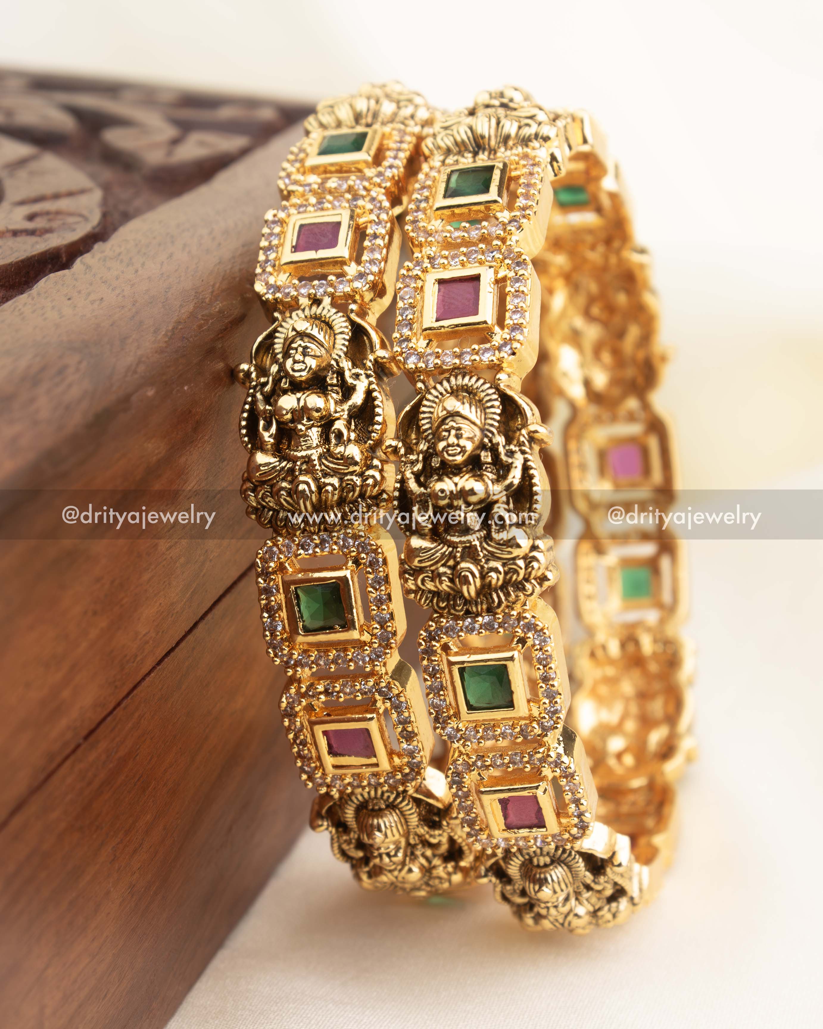 High-gold temple bangles with Nakshi deity panels and alternating green and ruby square stones.
