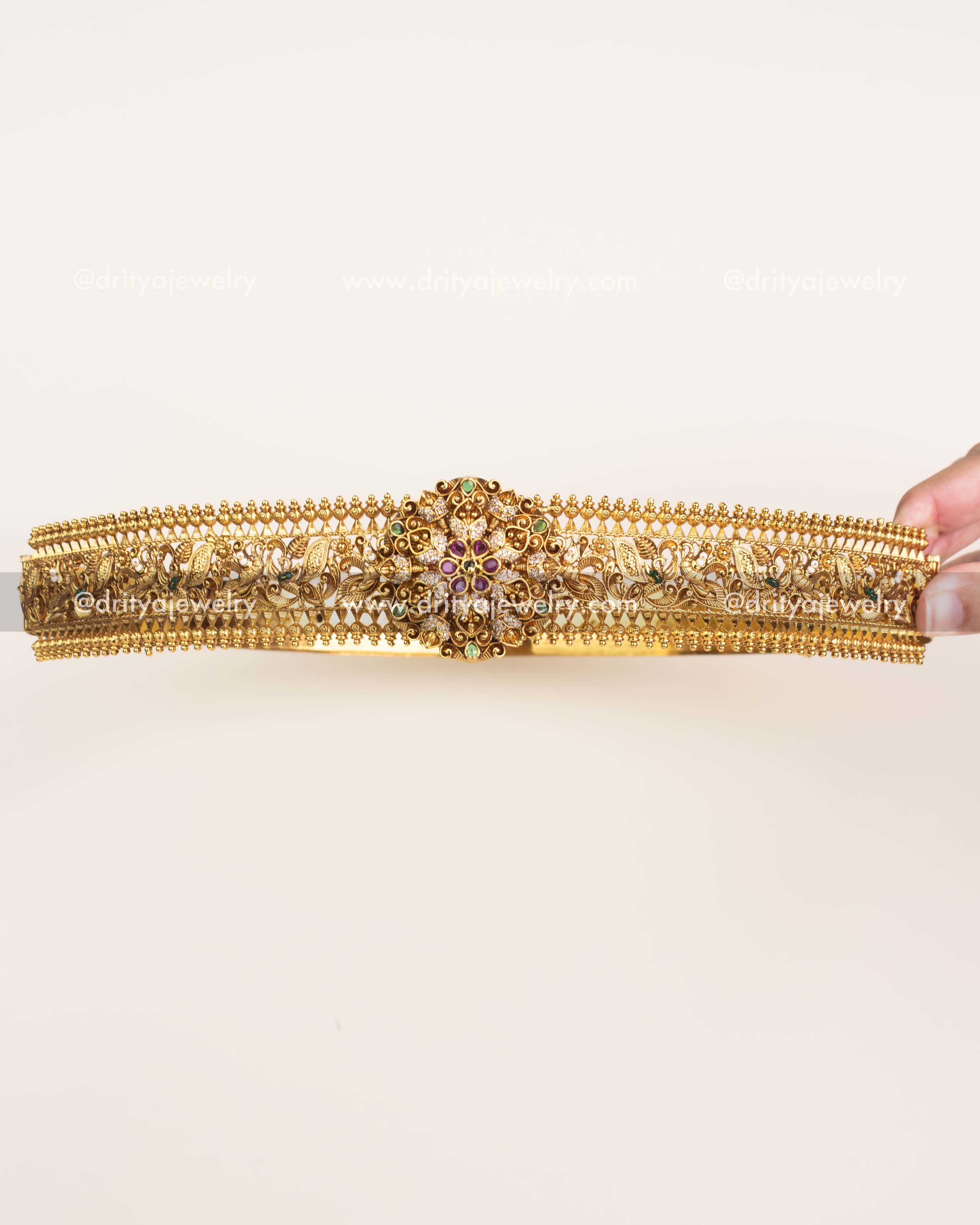 Antique gold traditional vadanam with floral centerpiece, ruby and emerald stone detailing.