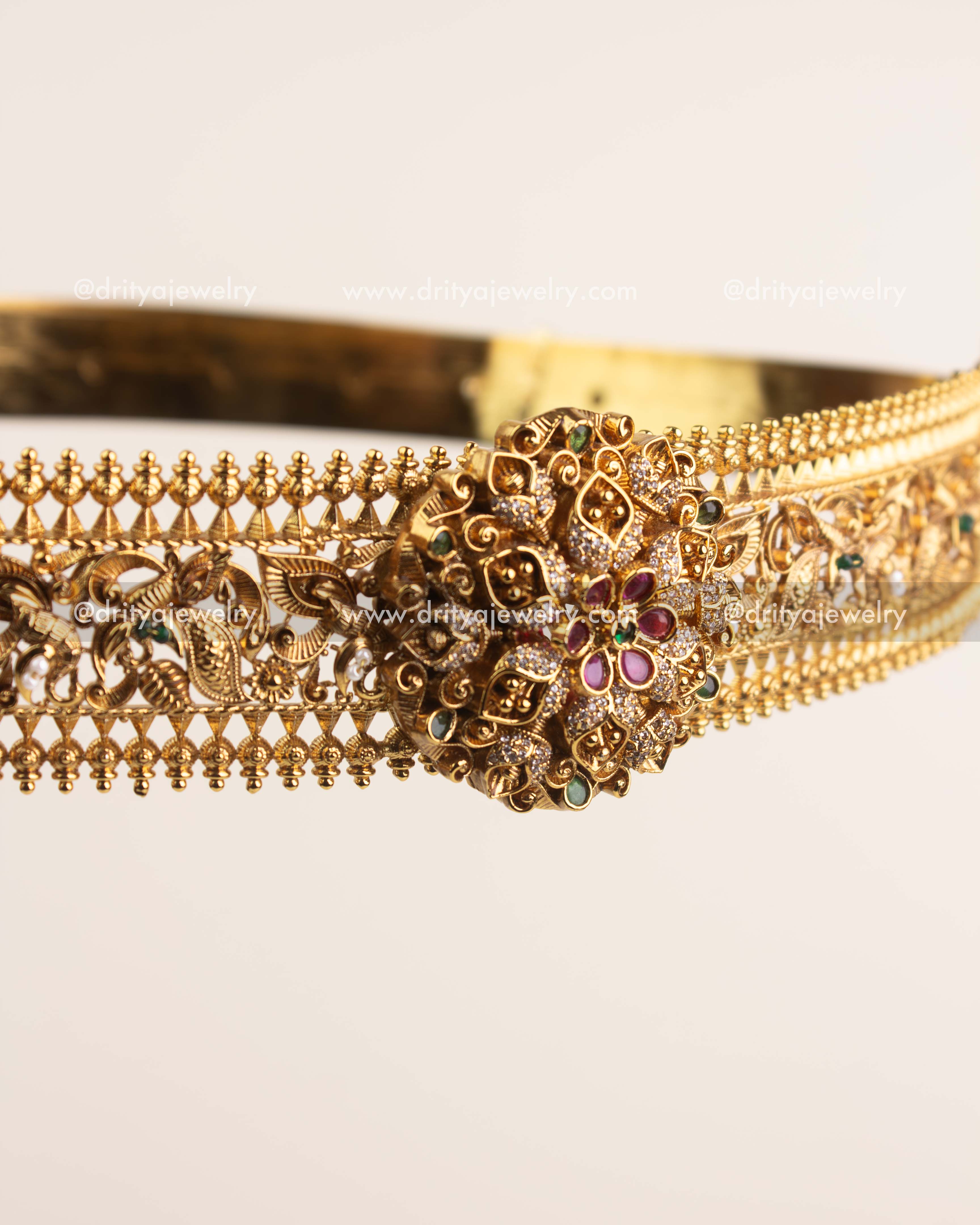 Handcrafted floral centerpiece of vadanam featuring ruby and emerald stones in antique gold finish.