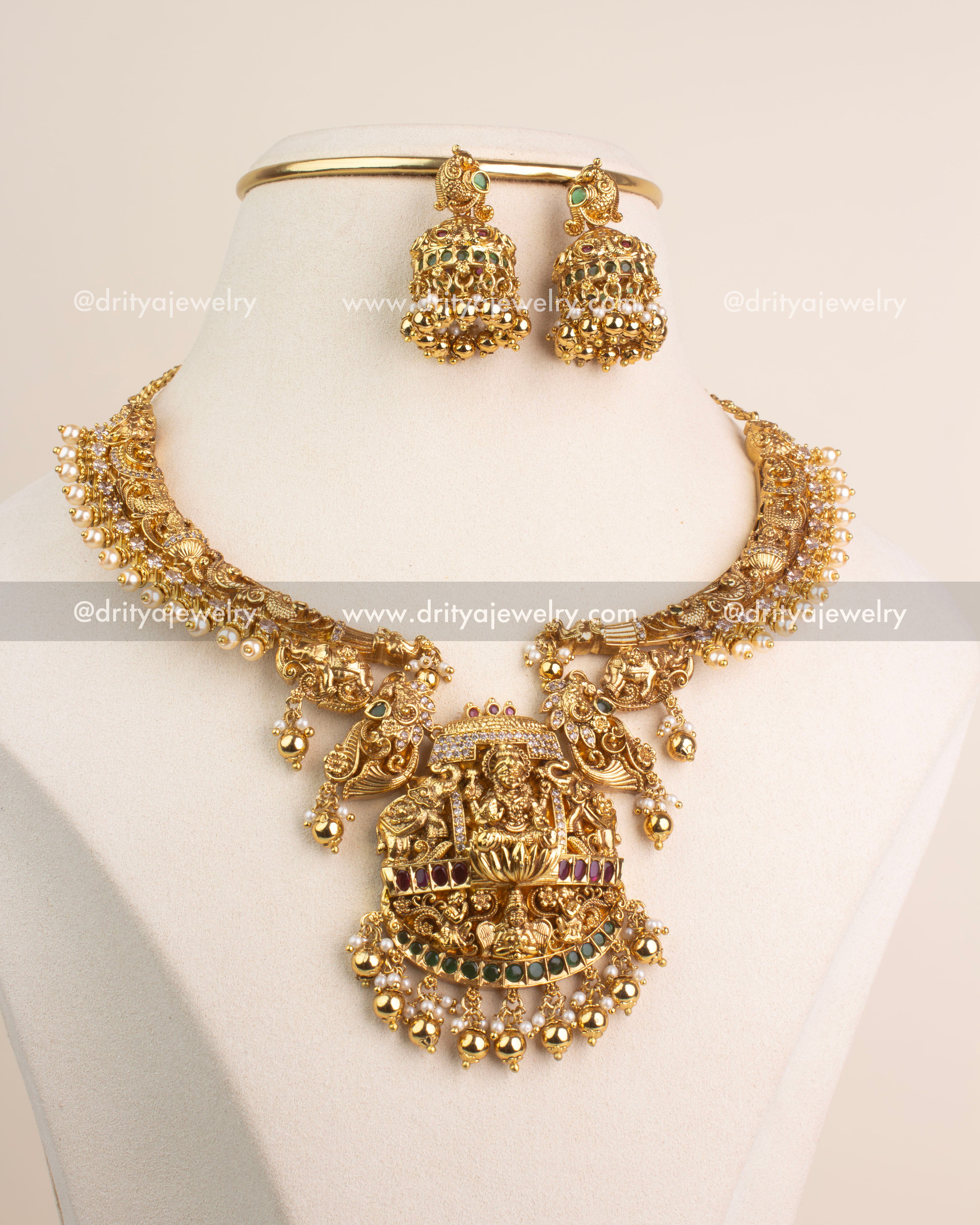 Antique gold short necklace with Lakshmi Devi pendant, ruby and emerald stones, and matching jhumkas.