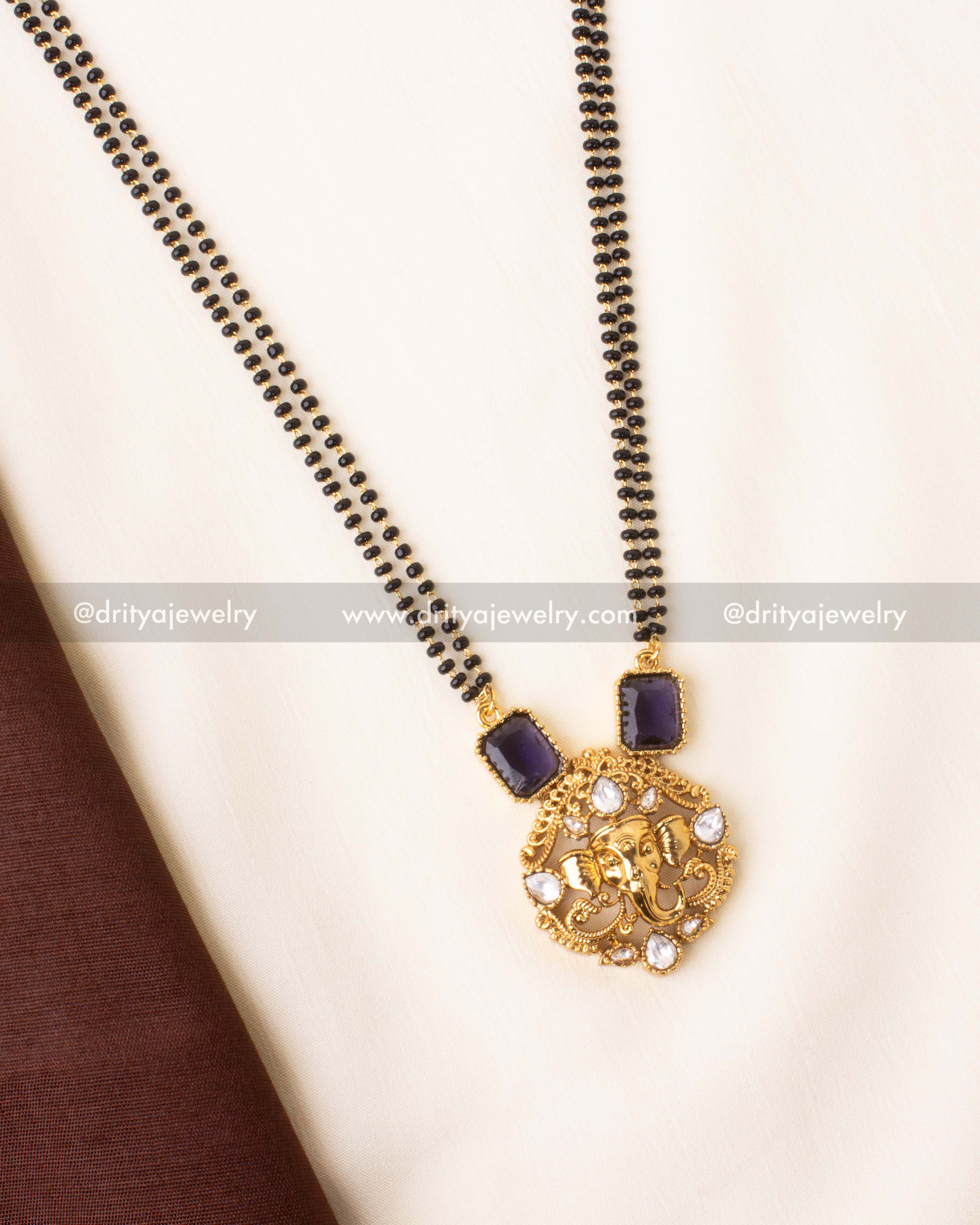 Gold-plated mangalsutra with purple stones and Ganesha motif pendant on black beads.