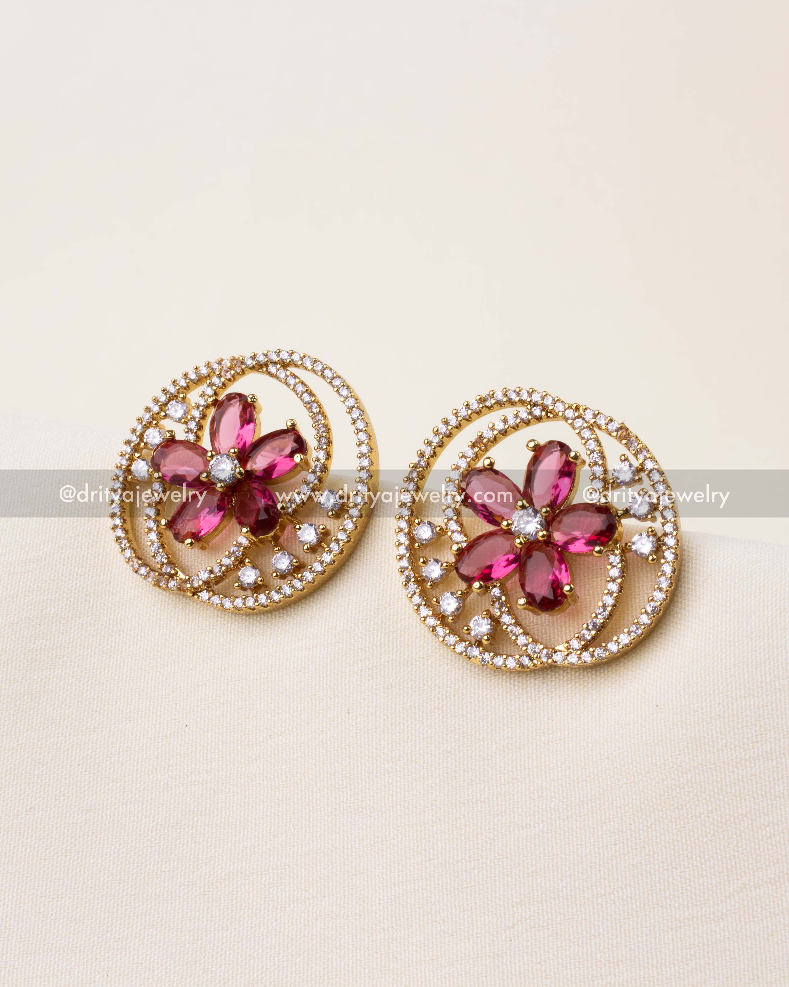 Gold-finished stud earrings with ruby red flower center and sparkling CZ spiral detailing.