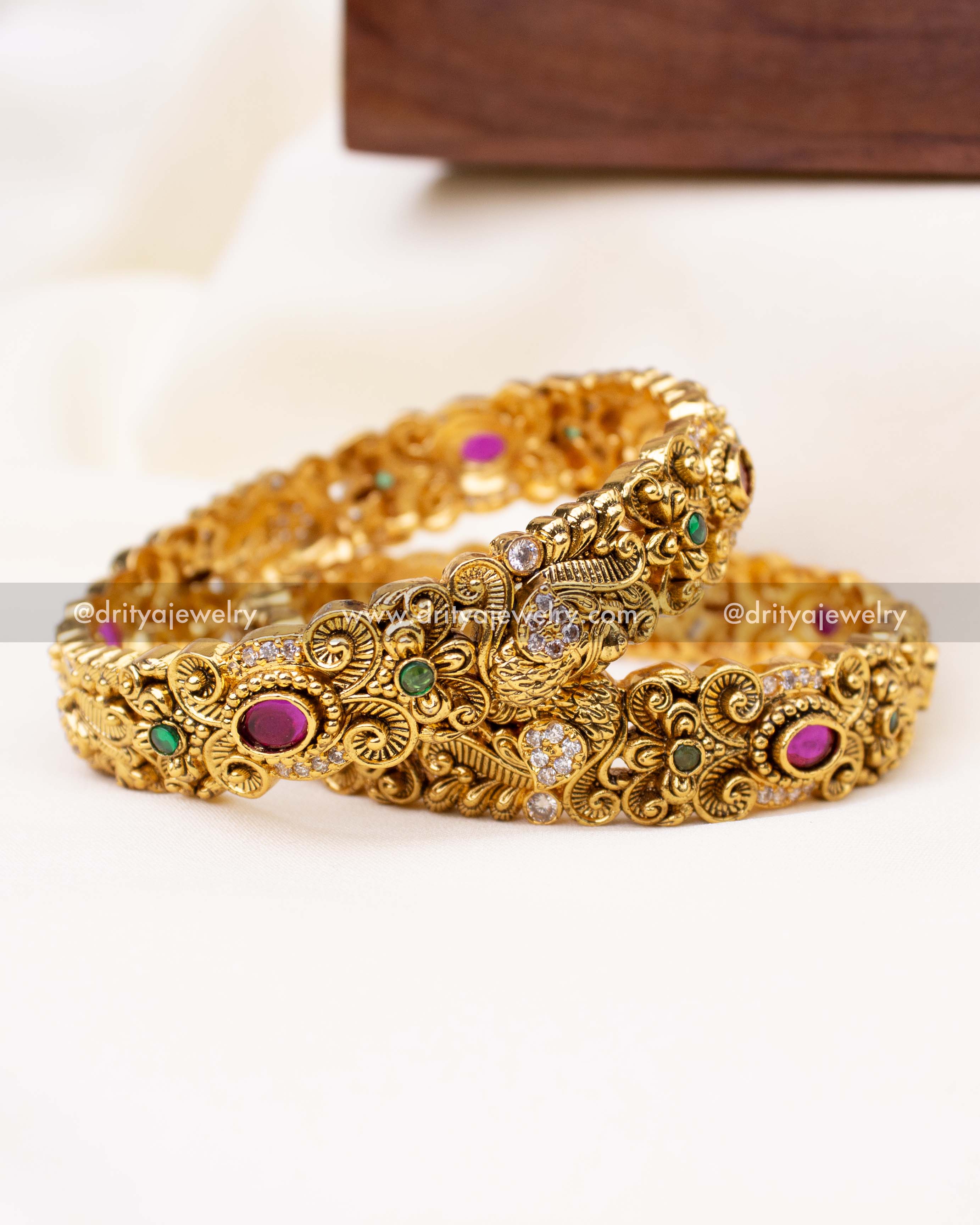 Detailed view of Nakshi-style bangles featuring floral carvings, ruby-green stones, and CZ highlights.