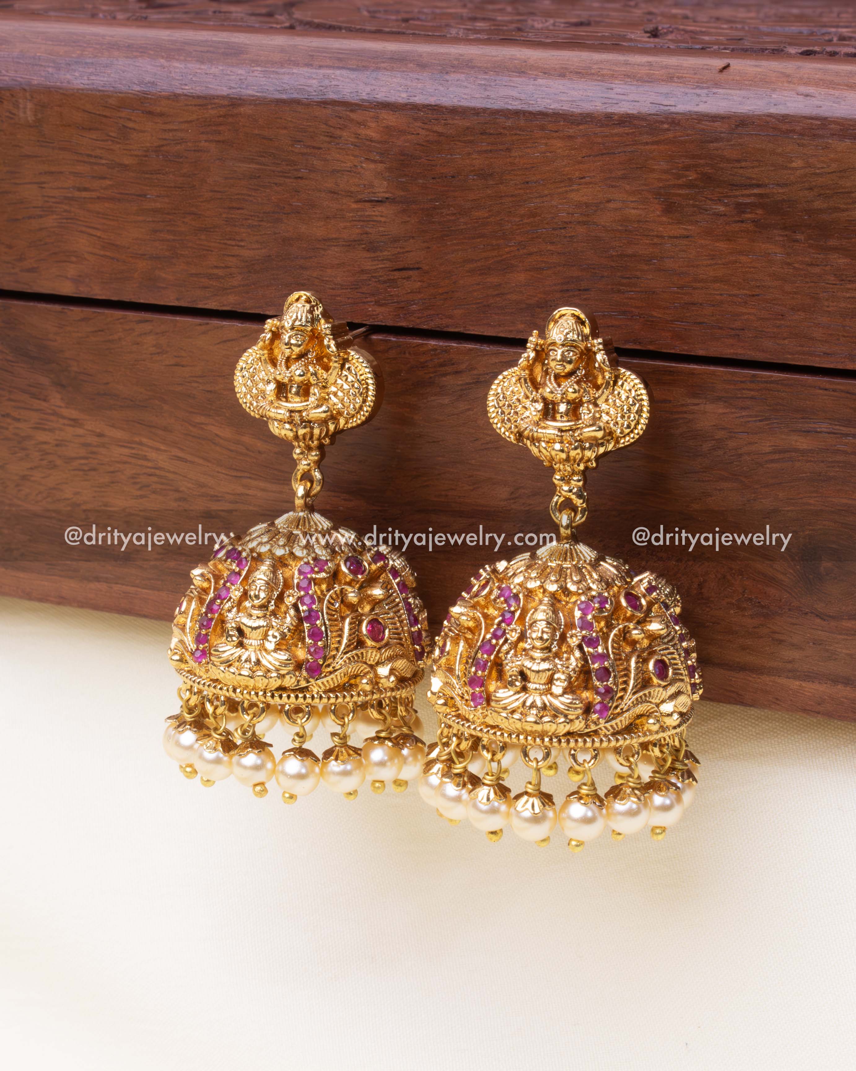Dome-shaped jhumkas with ruby red stones, intricate carvings, and pearl drops.