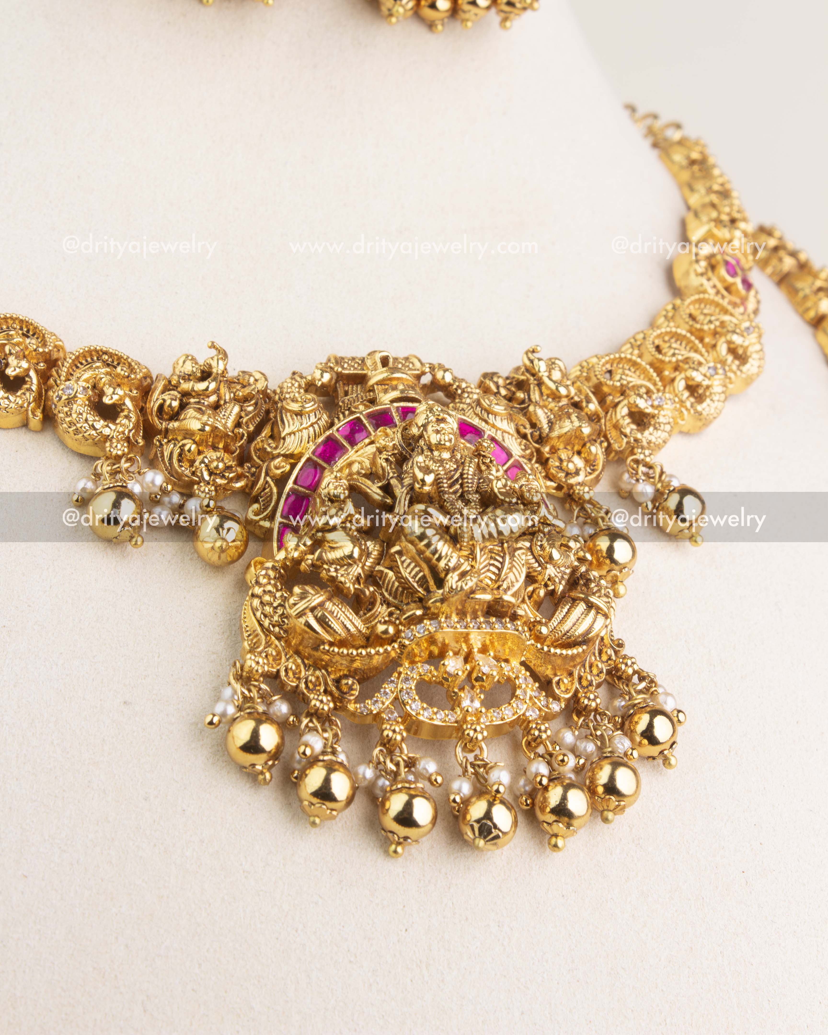 Detailed view of Lakshmi motif pendant with ruby kemp stones, peacock carvings, and pearl drops.