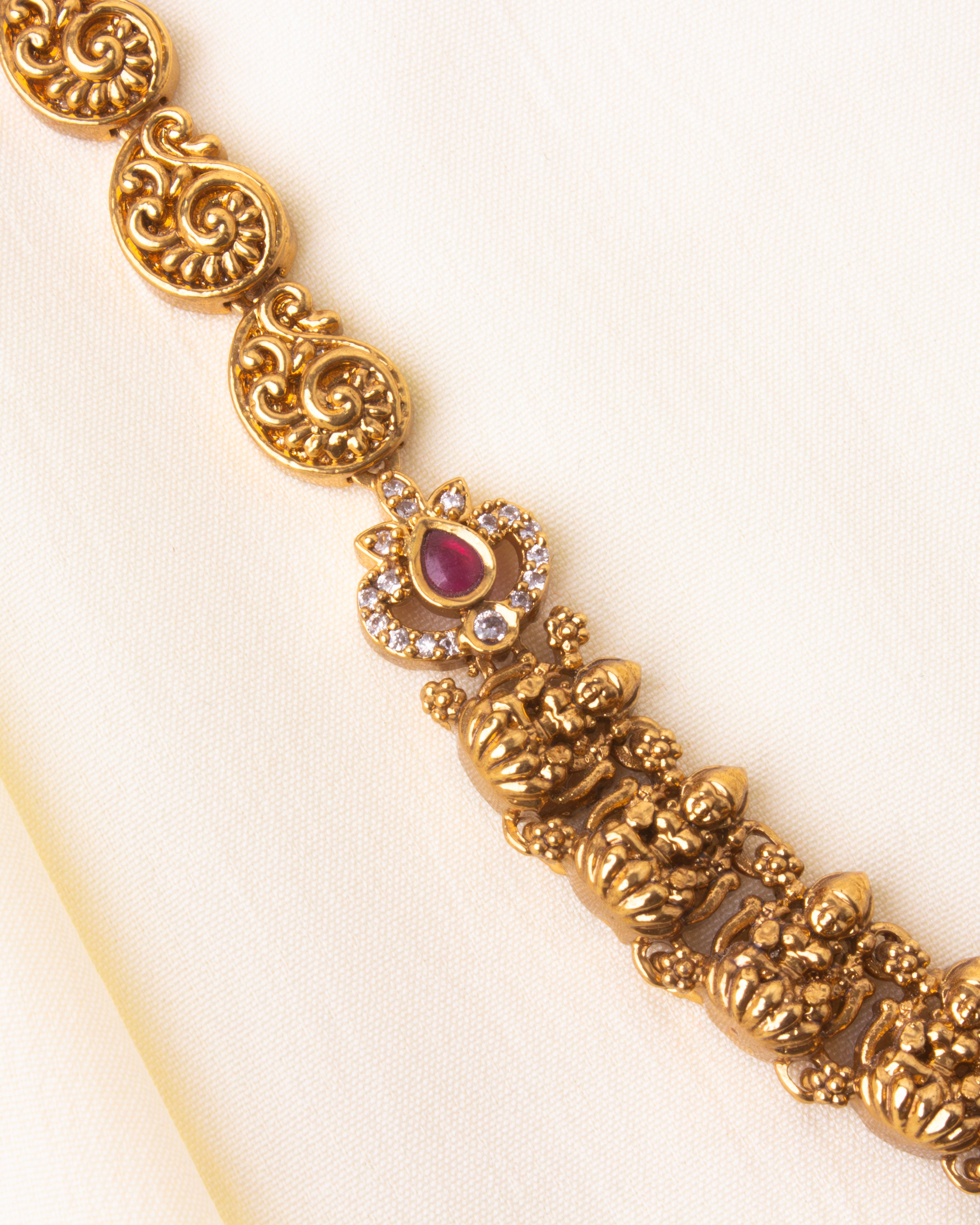 Close view of gold-finished temple chain with miniature Lakshmi motifs and ruby stone inlays.