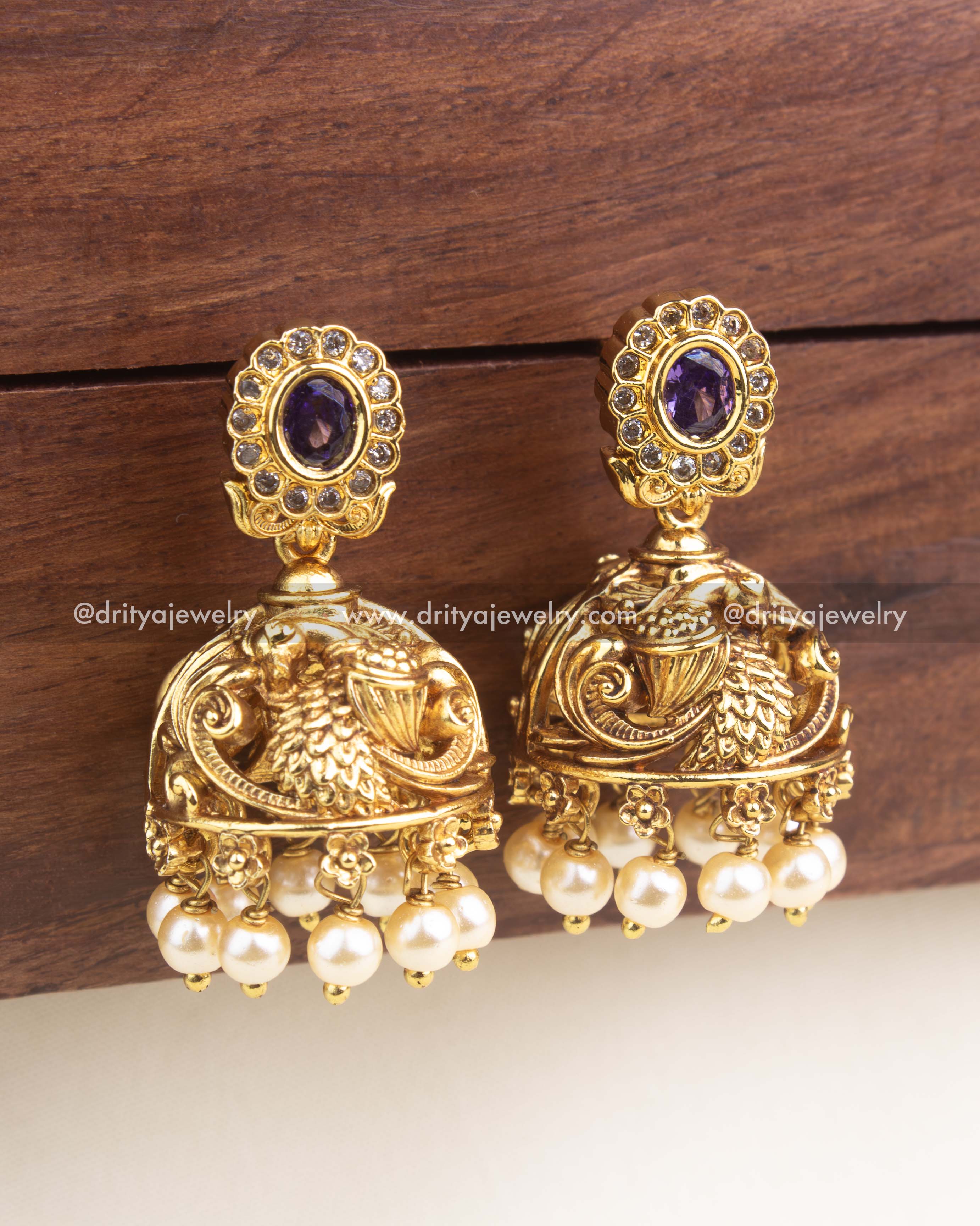 Temple-style jhumka with embossed peacock detailing, pearl clusters, and oval purple stone stud.