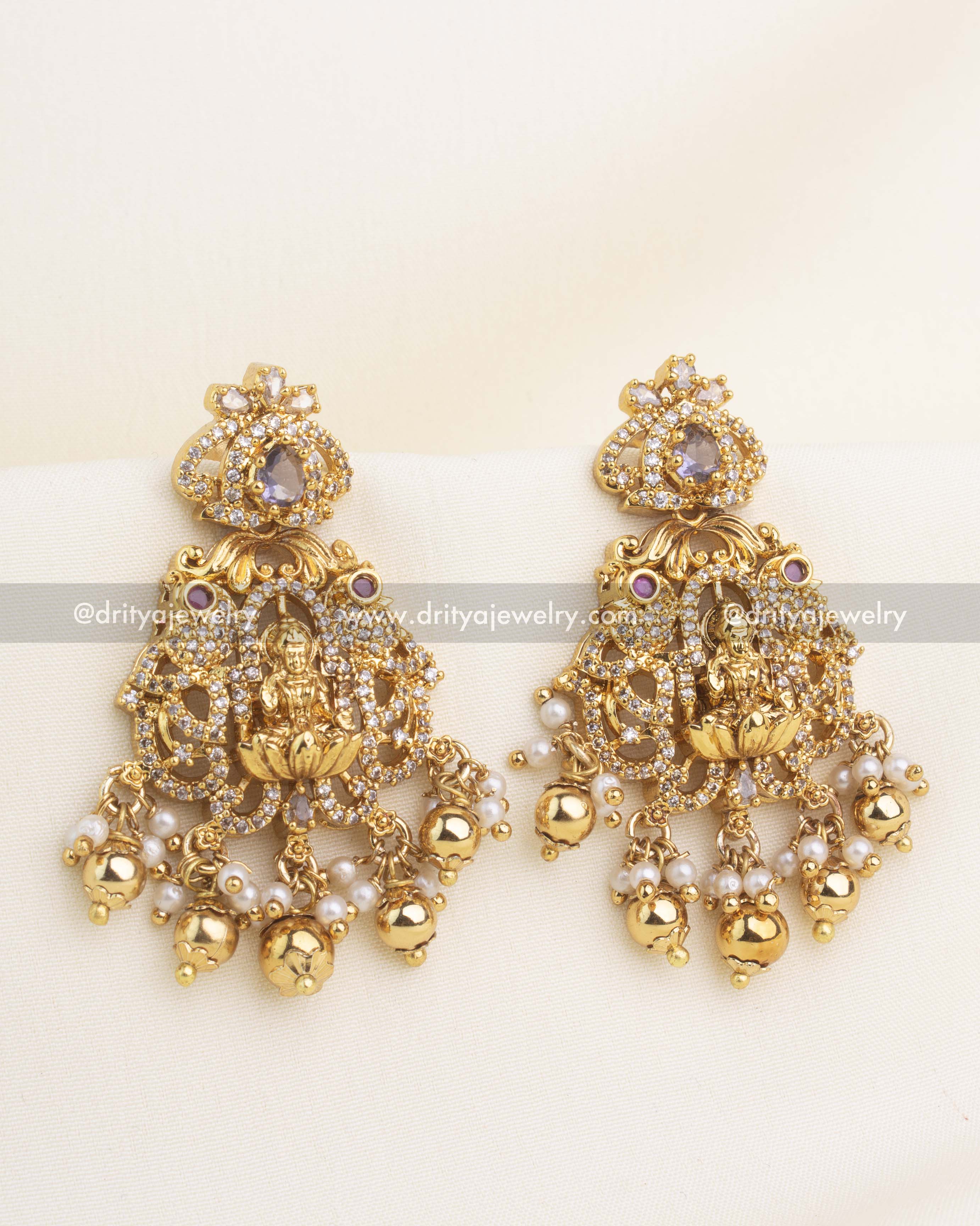 Pair of temple earrings with Lakshmi motif, purple CZ stones, and pearl-gold drops.