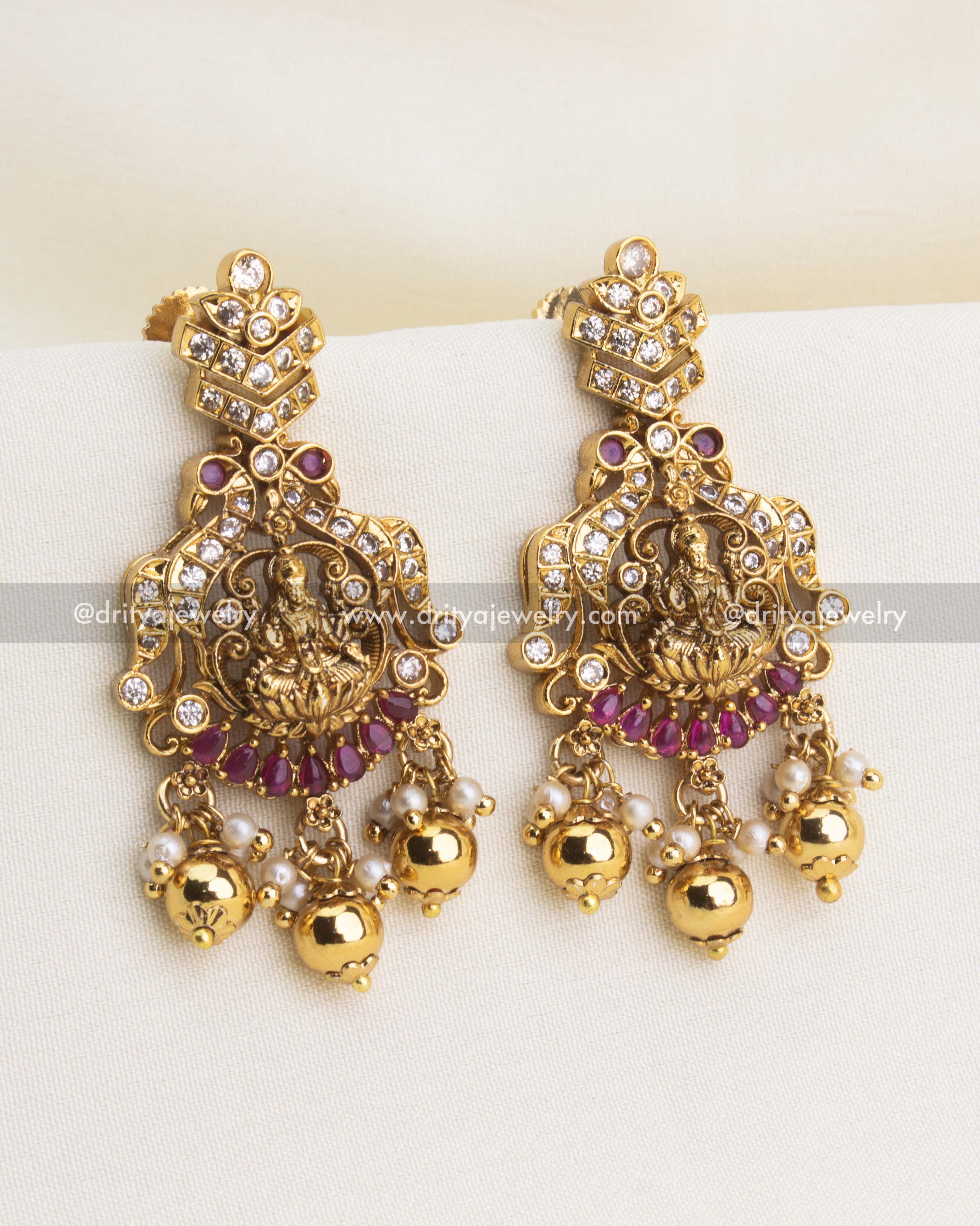 Traditional temple earrings with Lakshmi carving, CZ highlights, red stones, and pearl clusters.