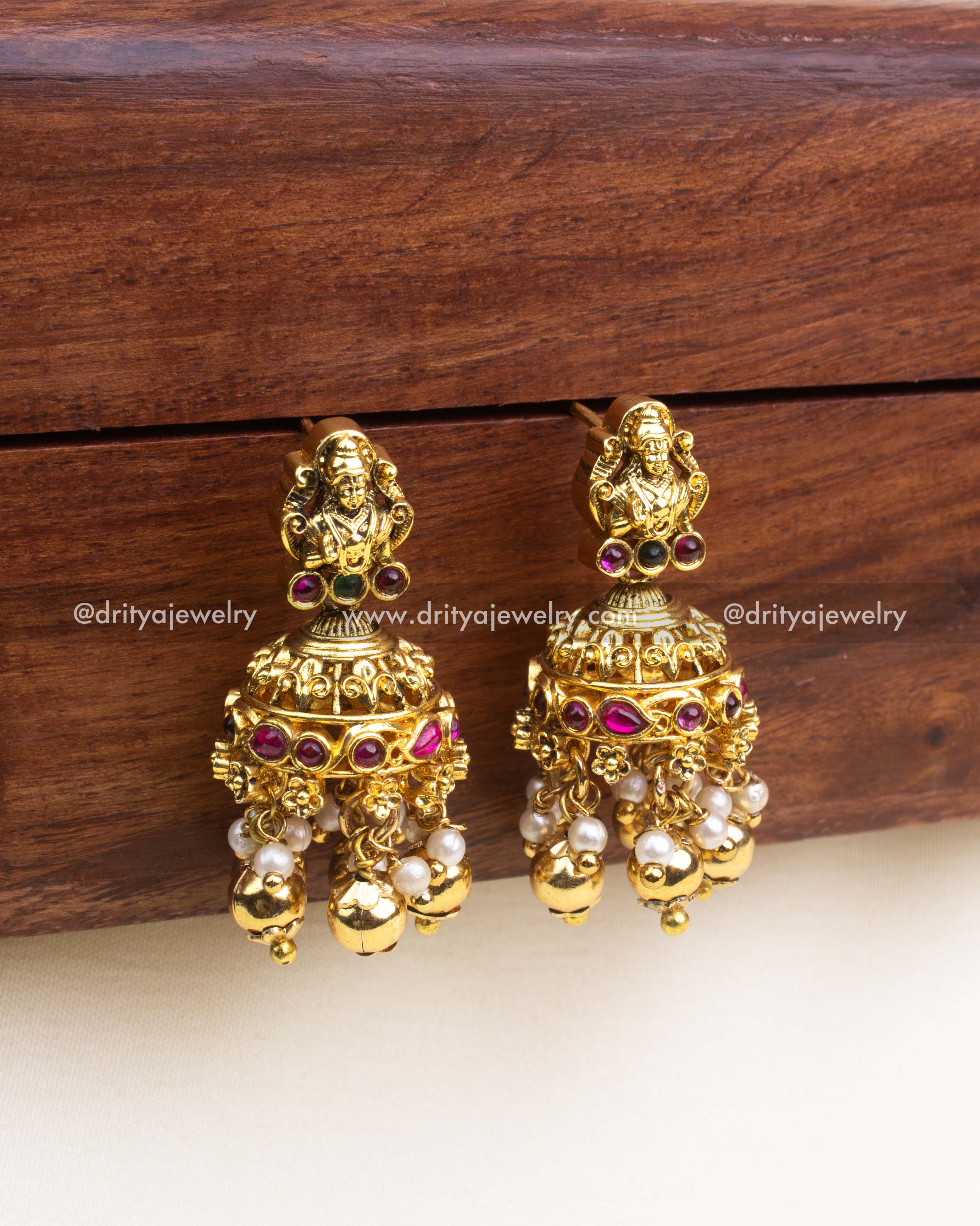 Gold temple jhumka earrings with deity top, kemp inlay and pearl–ball danglers in antique finish.