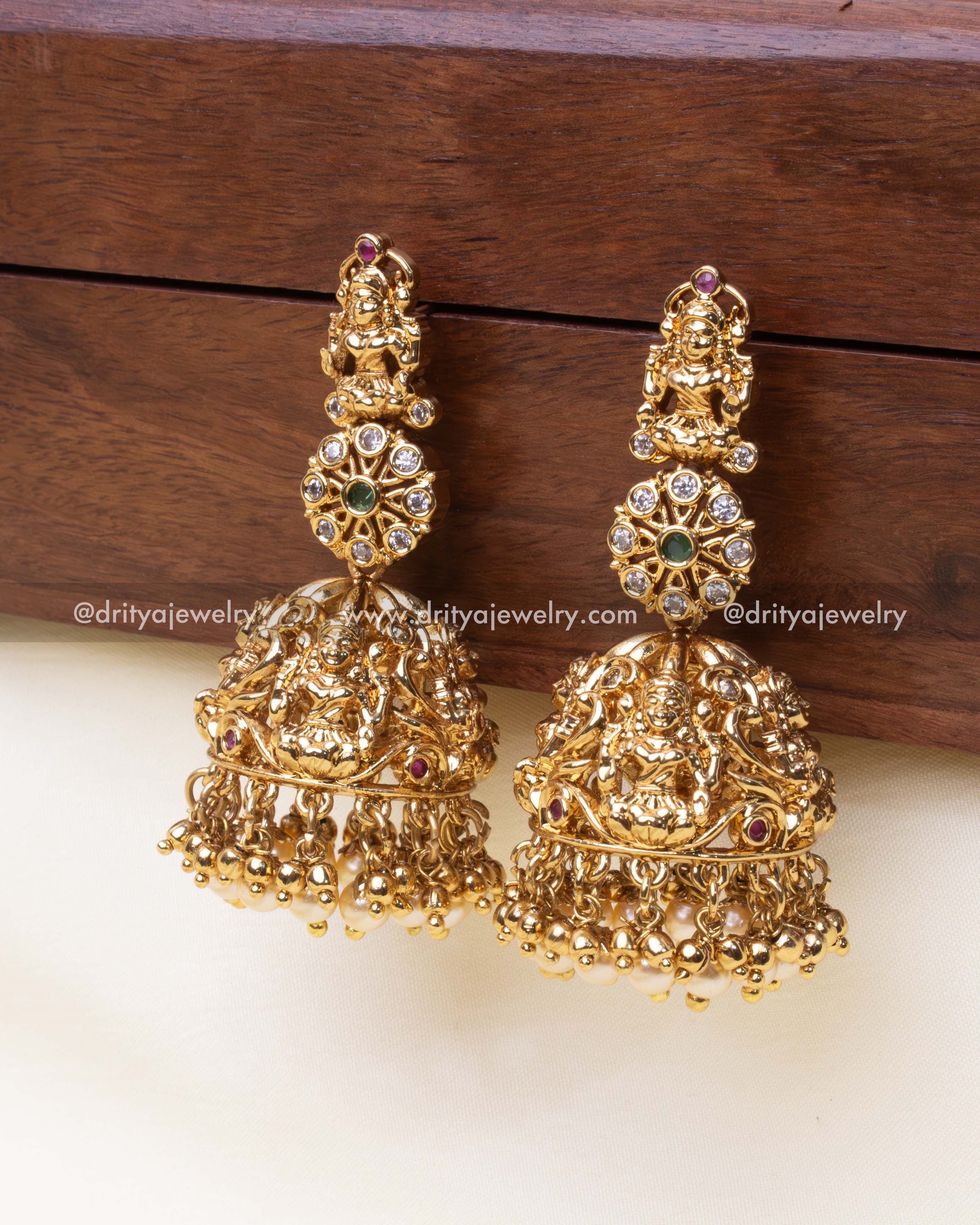 Traditional Nakshi Jhumkas with deity engravings, pearl drops, and antique gold finish, perfect for weddings and festivals.
