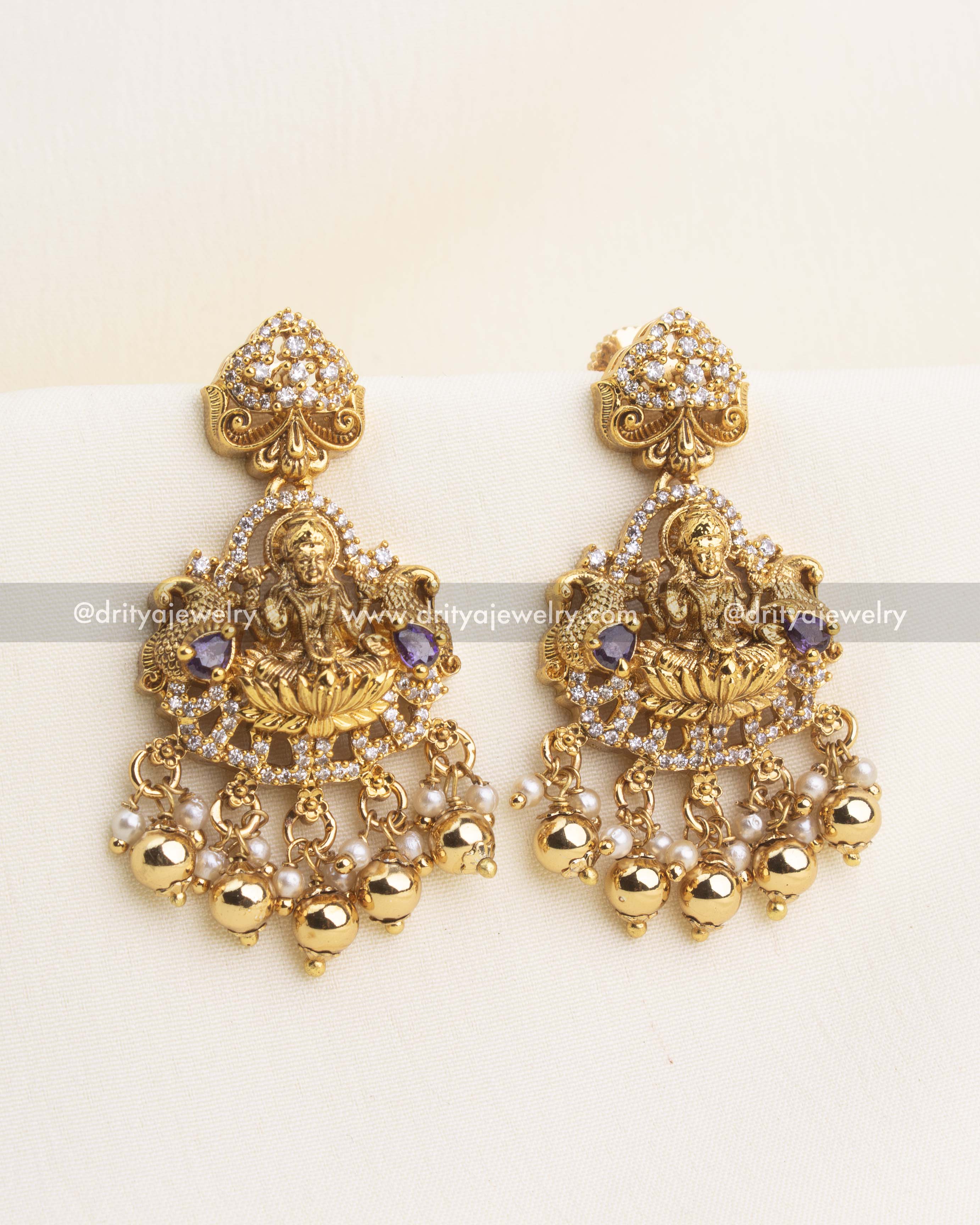 Pair of temple-style earrings with Lakshmi motif, CZ stones, purple accents, and pearl bead hangings