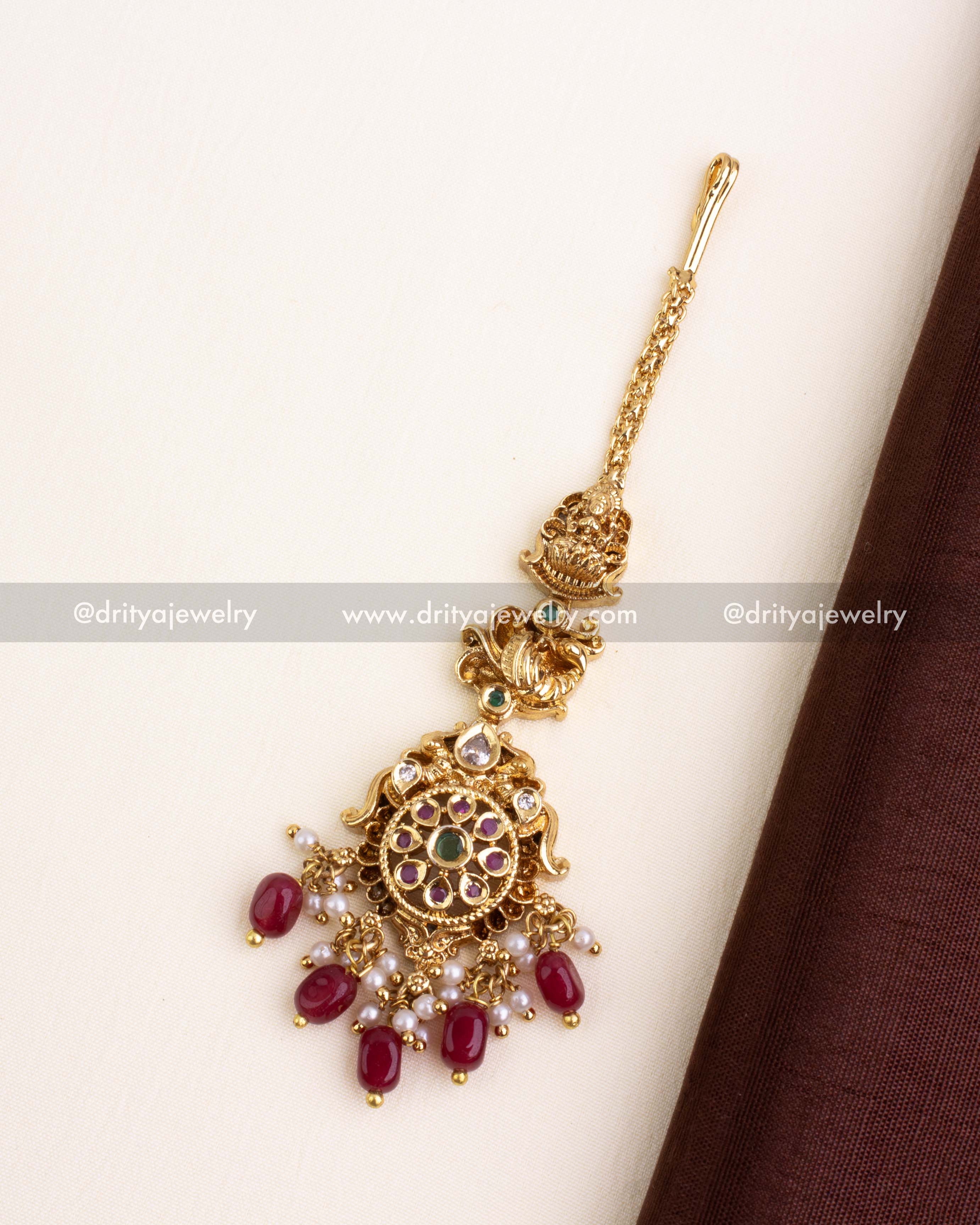 Antique gold temple maang tikka with circular design and hanging ruby red beads.