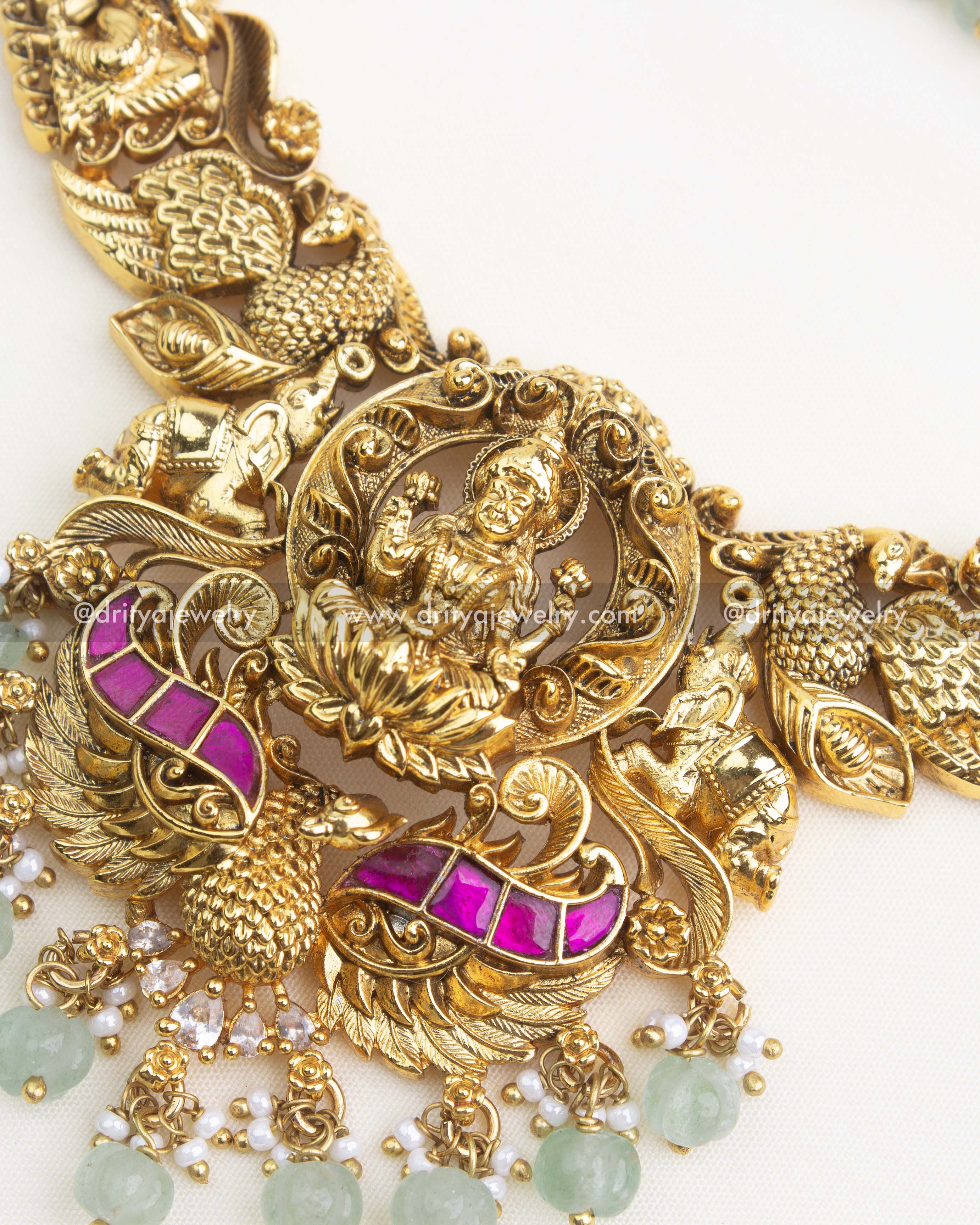 Close-up of Goddess Lakshmi pendant with pink kemp stones, peacock motifs, and green bead hangings