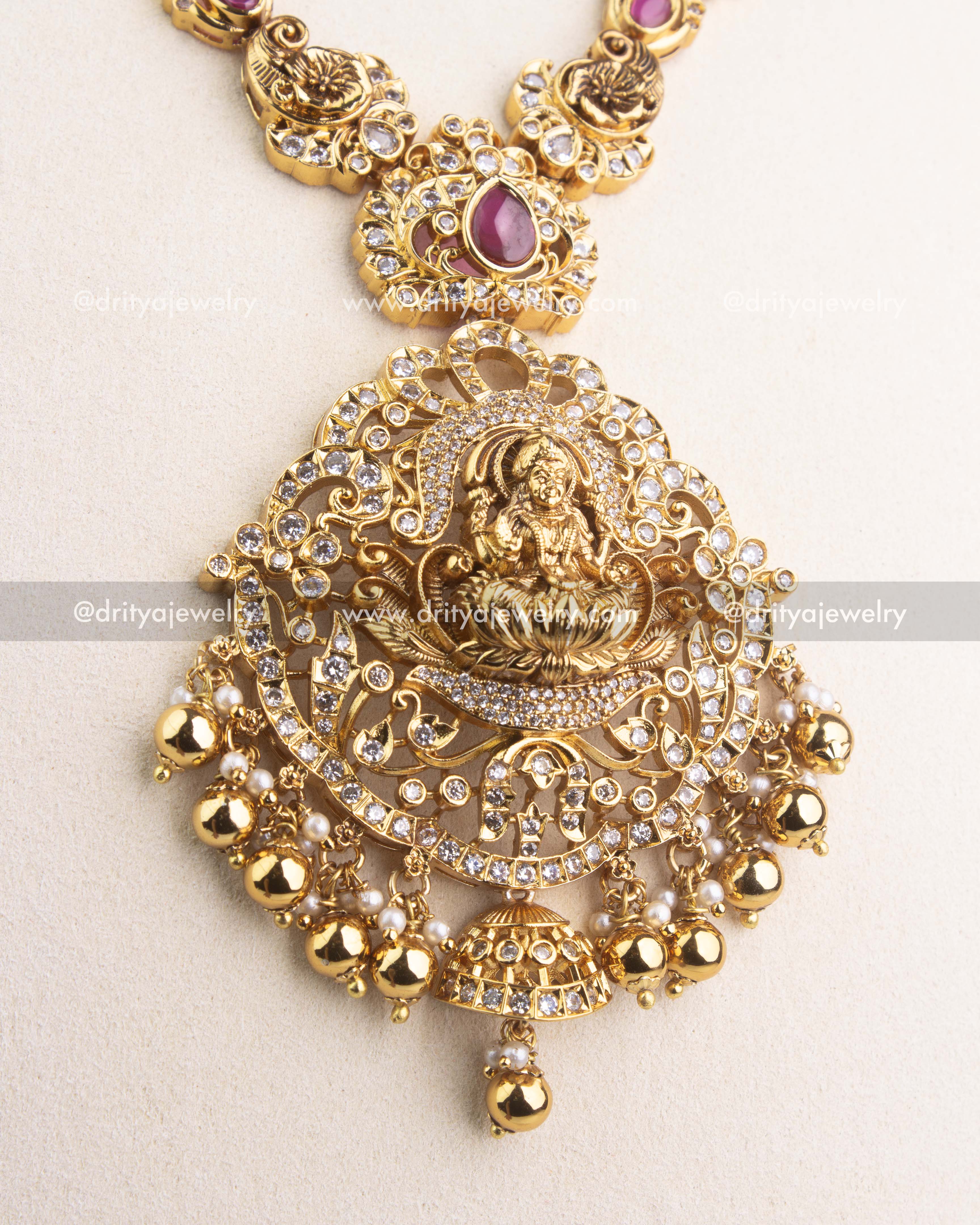 Intricate Lakshmi Devi pendant with CZ and ruby detailing in antique gold finish.