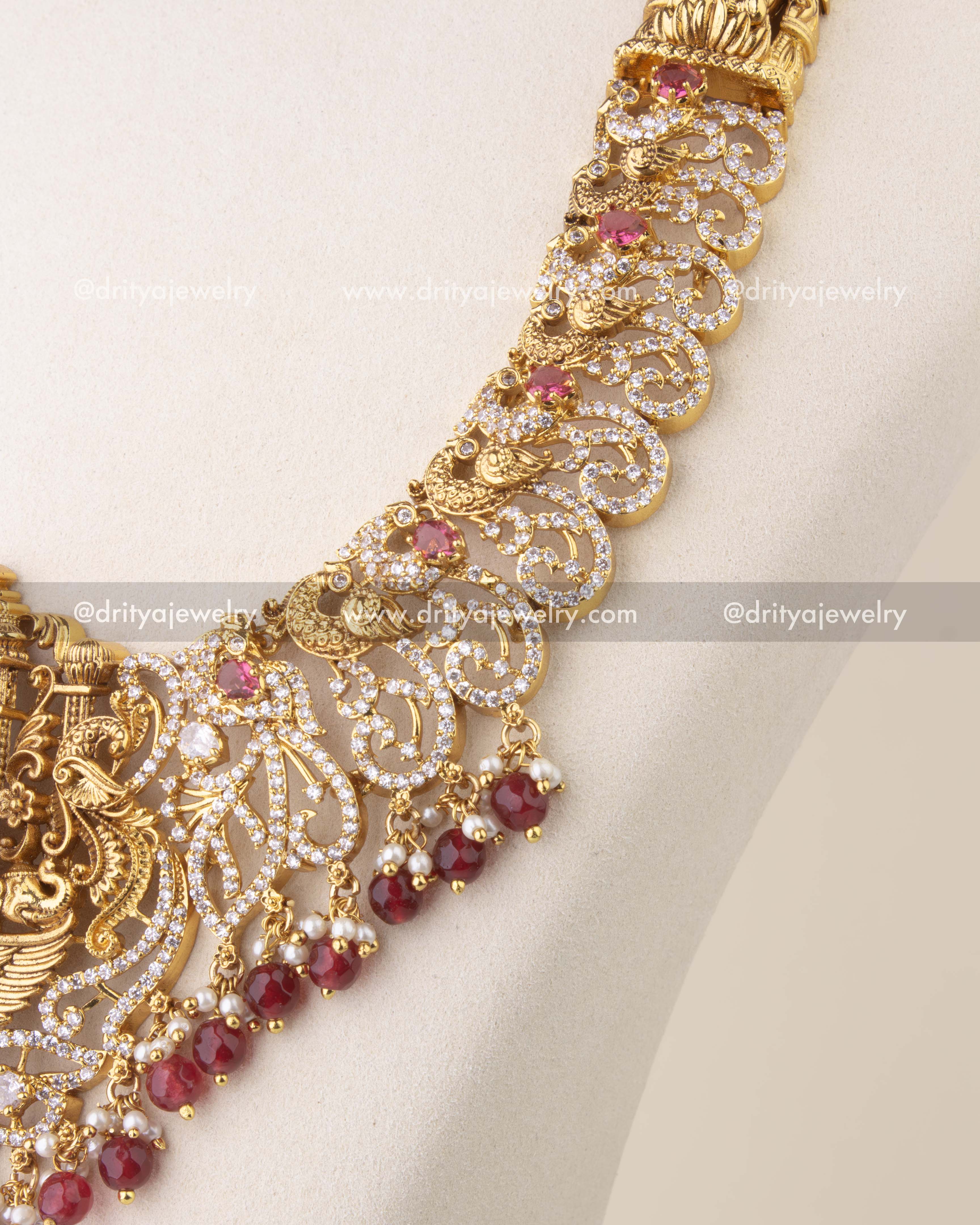 Close-up of Nakshi temple necklace with ruby red stones, peacock motifs, and antique gold finish.