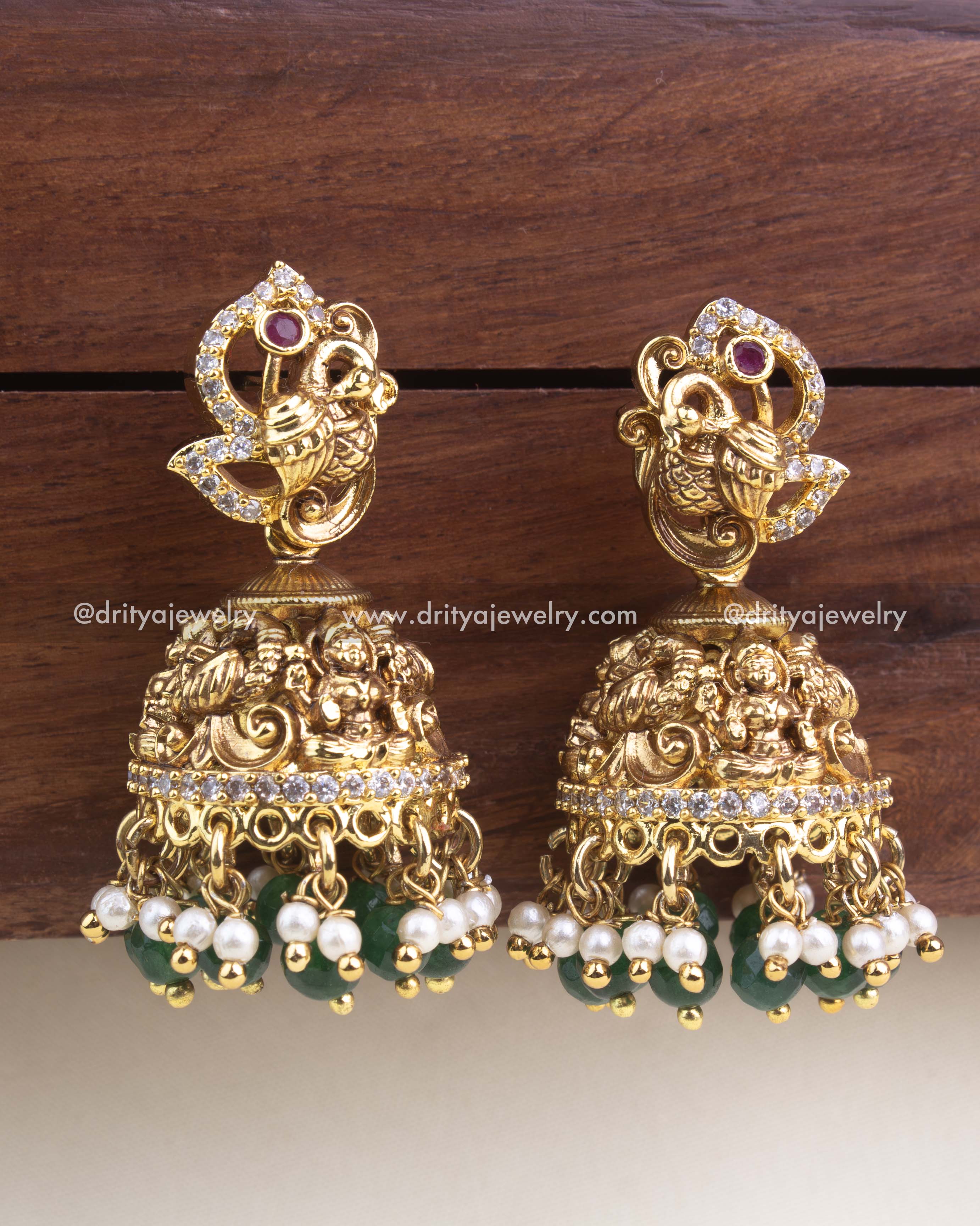 Antique gold peacock jhumkas with nakshi detailing, CZ accents, green beads, and pearl hangings.