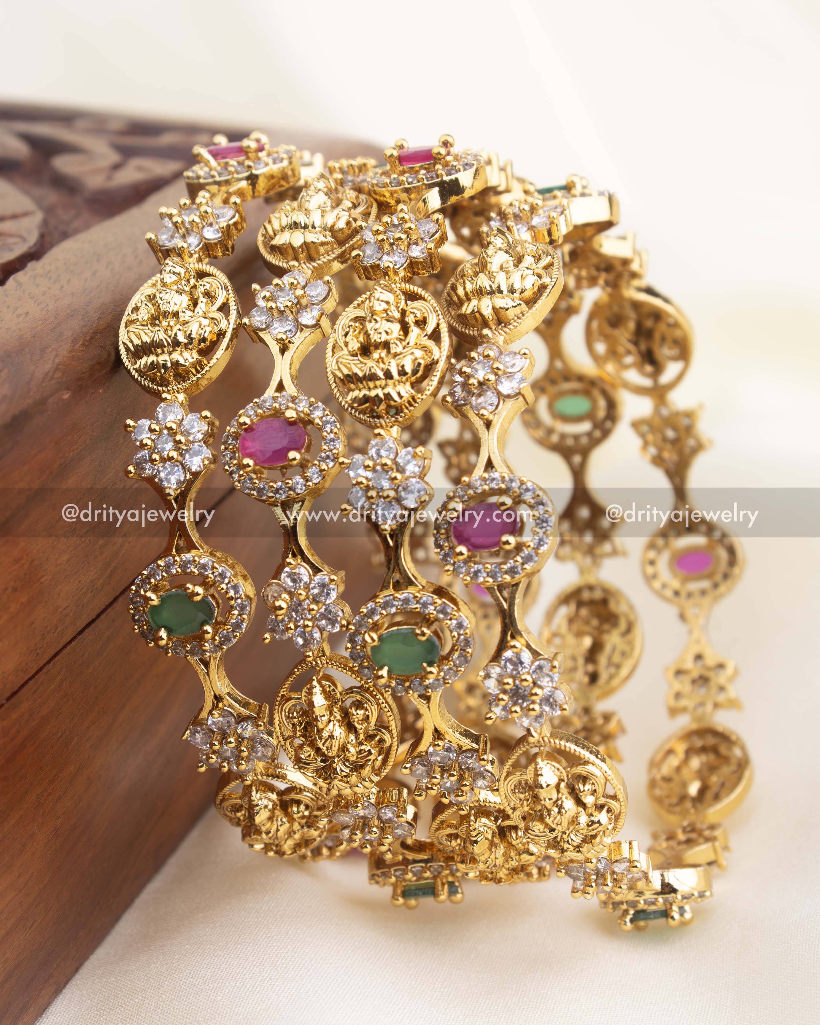 Close-up of premium temple bangles with intricate deity engravings, ruby and green stone mix, and high-shine CZ clusters.