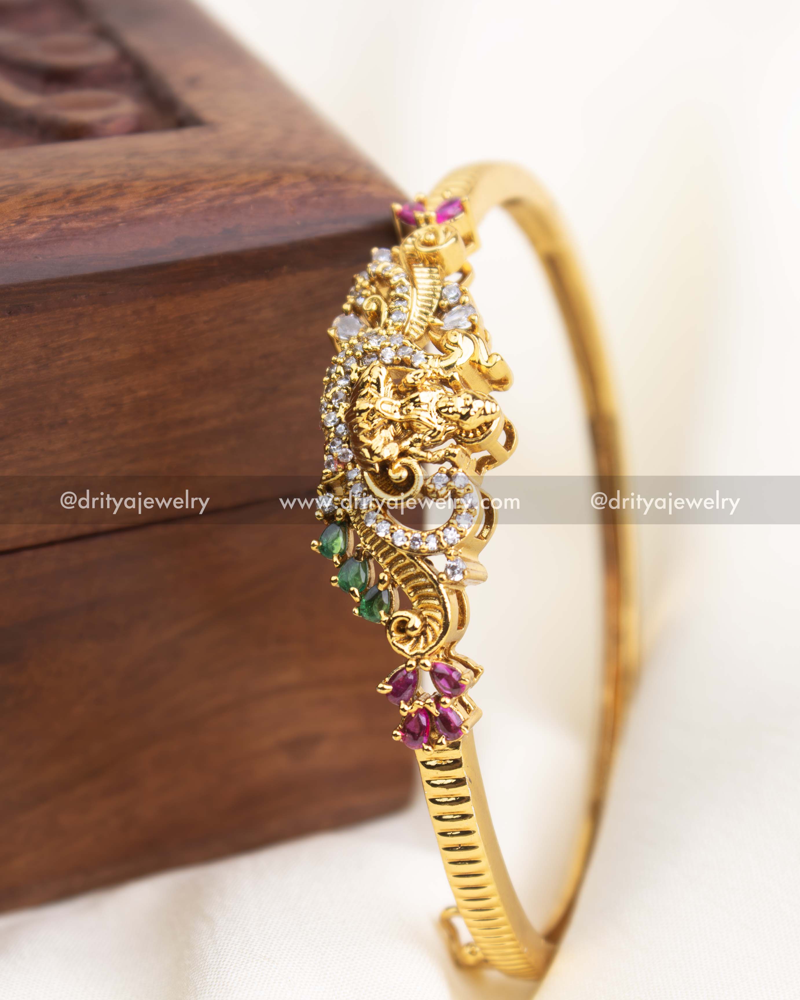 Close-up image of temple kada showcasing nakshi carving, CZ stones, ruby and emerald accents.