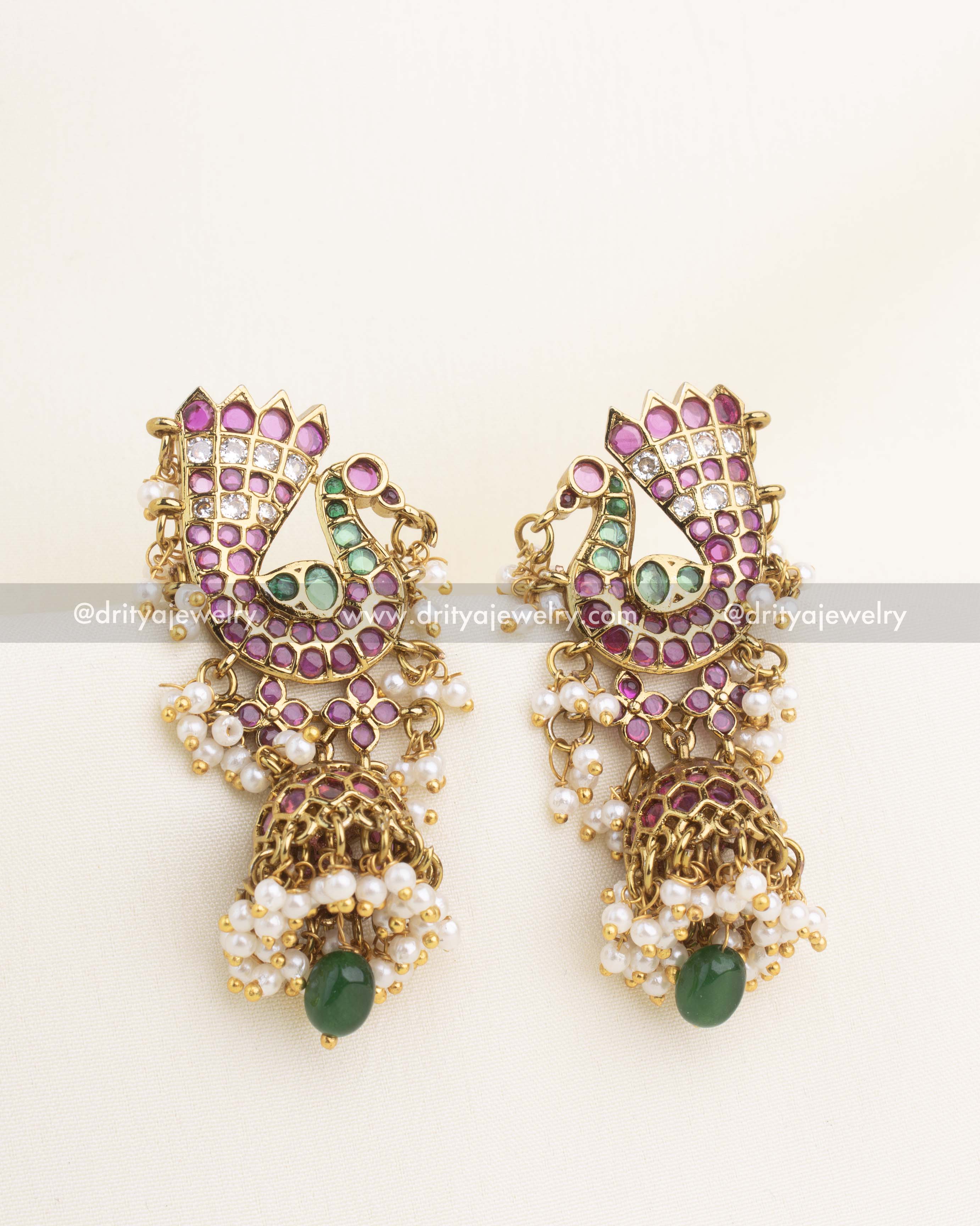 Stone-studded peacock earrings featuring kundan work, pearl clusters, and green bead drop.