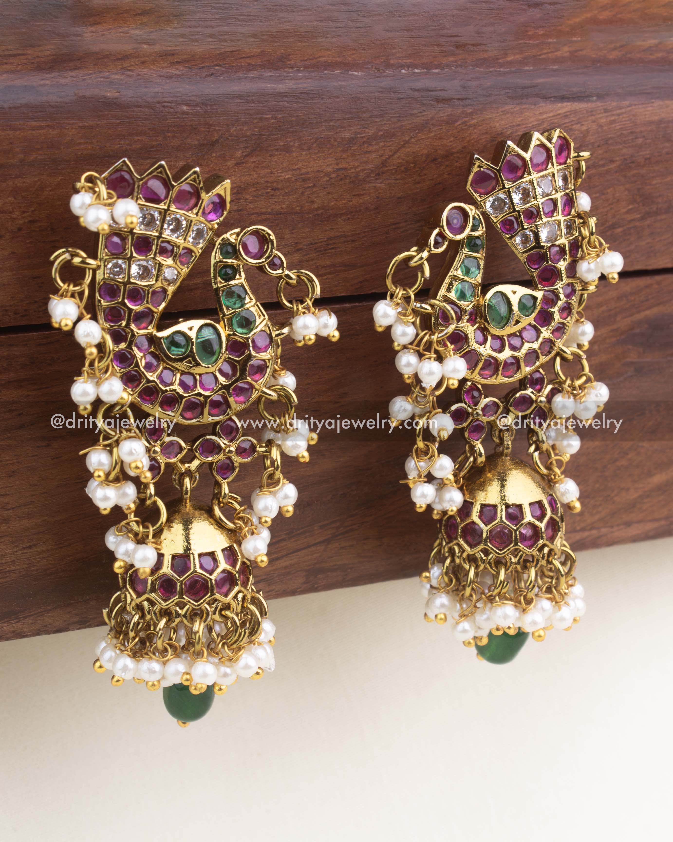 Premium gold-finish peacock dangler earrings with ruby and emerald stones, mini jhumka, and pearl drops.