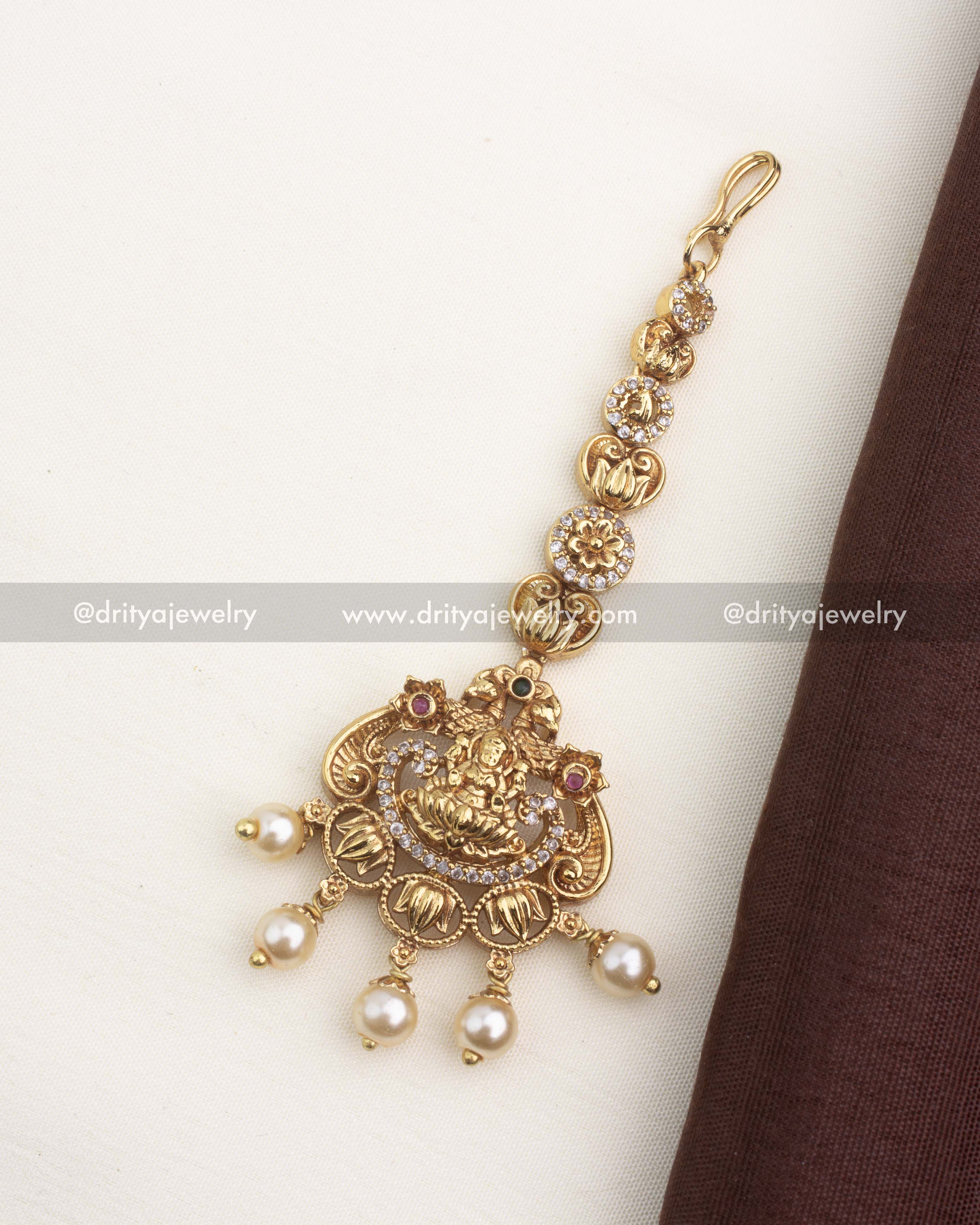 Traditional temple-style maang tikka with Lakshmi motif, CZ stones, and pearl danglers in antique gold finish.