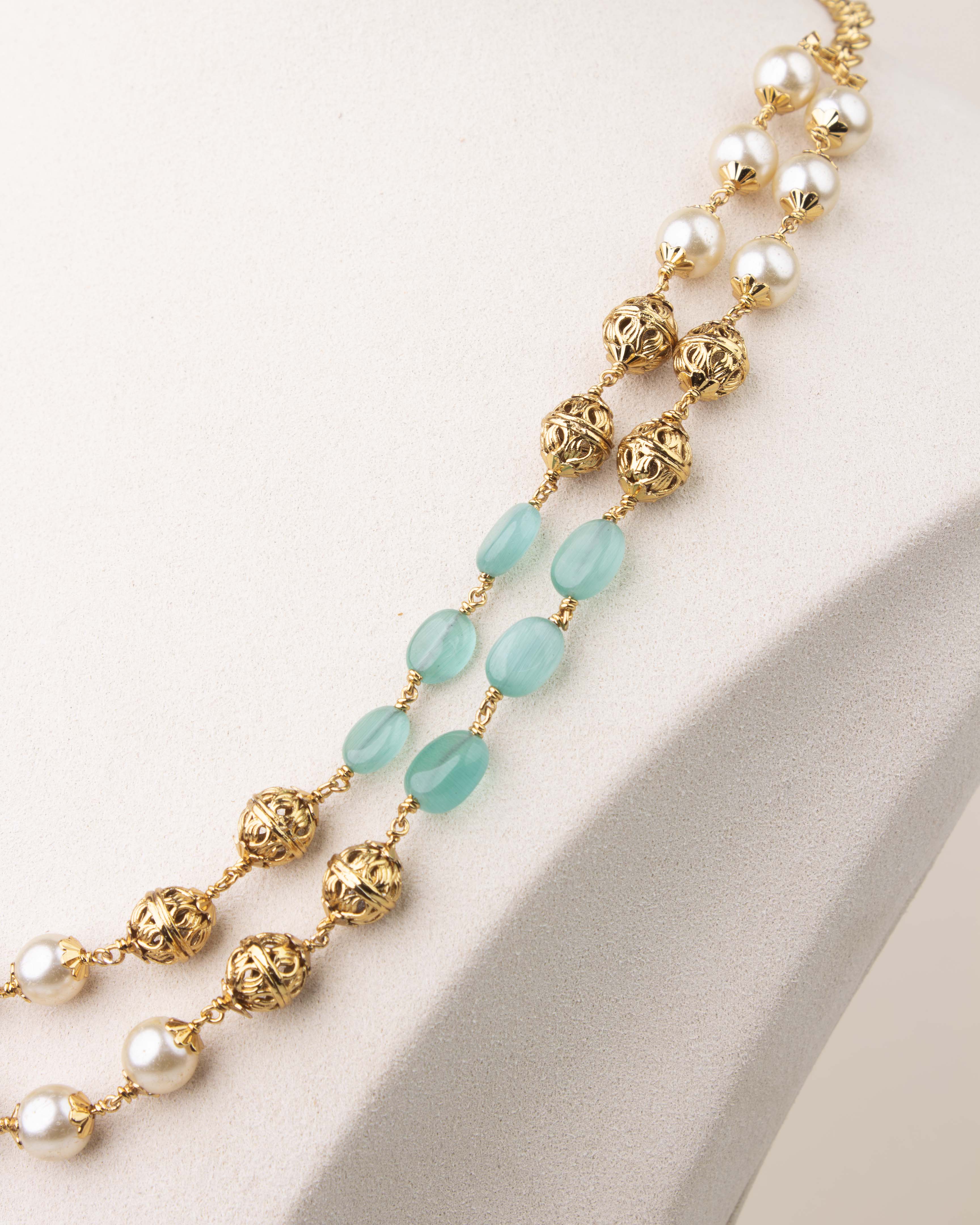 Close-up of mint green beads and pearls with gold polish detailing in layered mala necklace