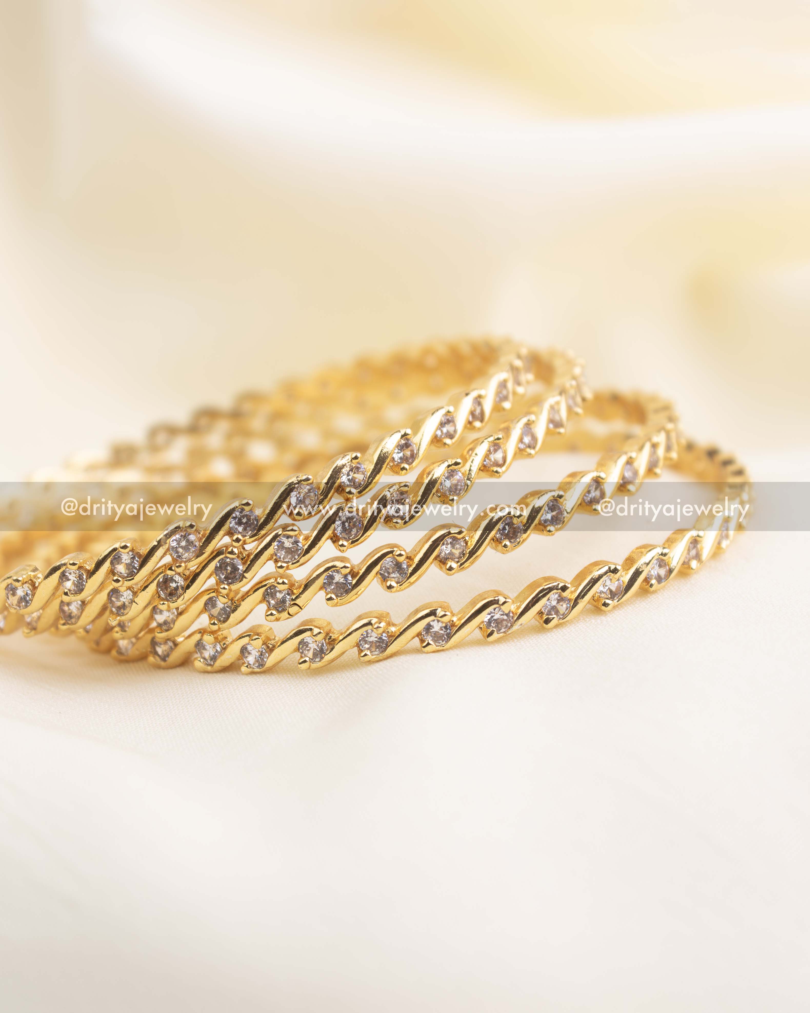 Close-up of wave-design CZ bangles showcasing detailed stone placement and gold finish.
