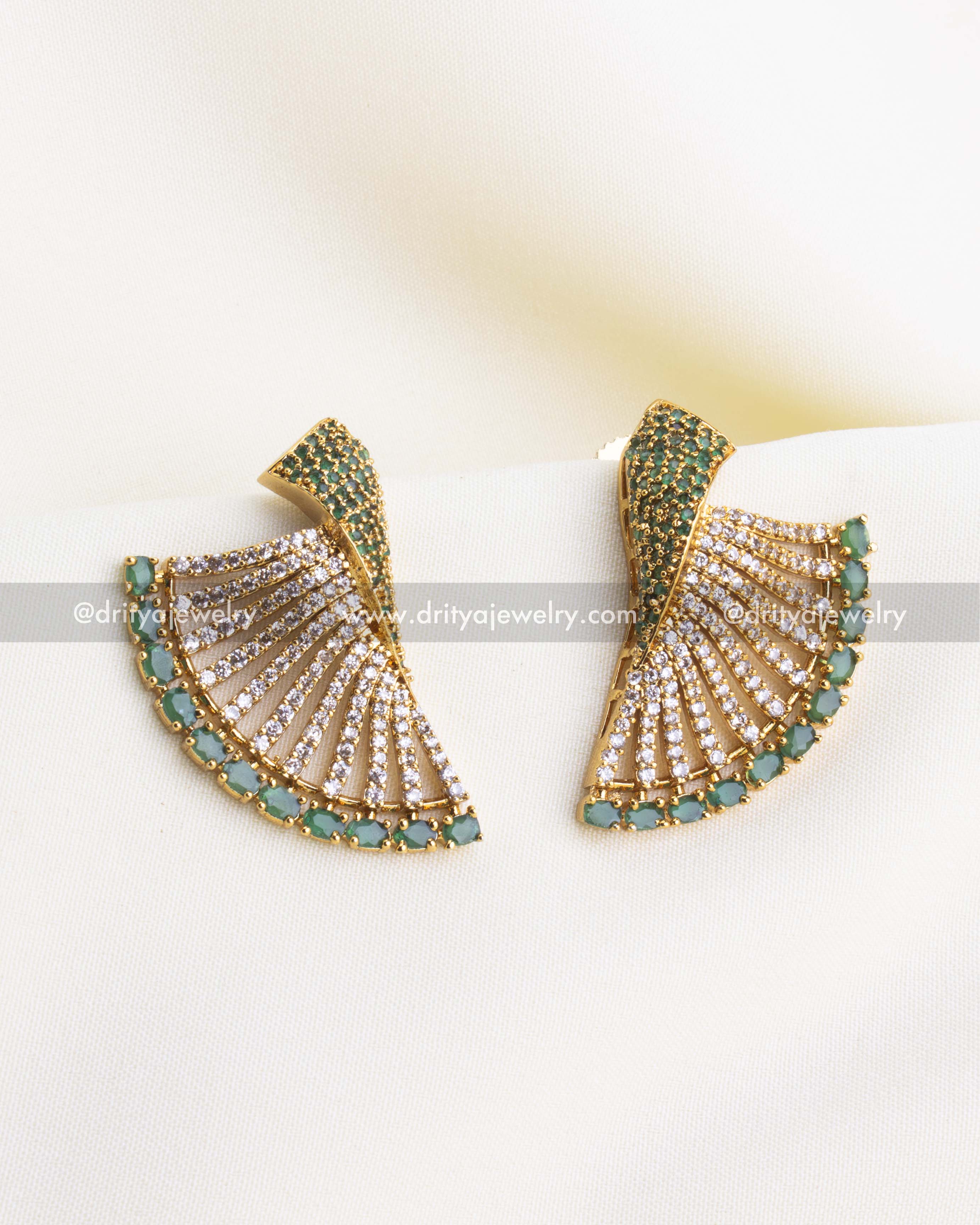 SKU 1119-G emerald and CZ fan-shaped designer earrings front view on fabric backdrop