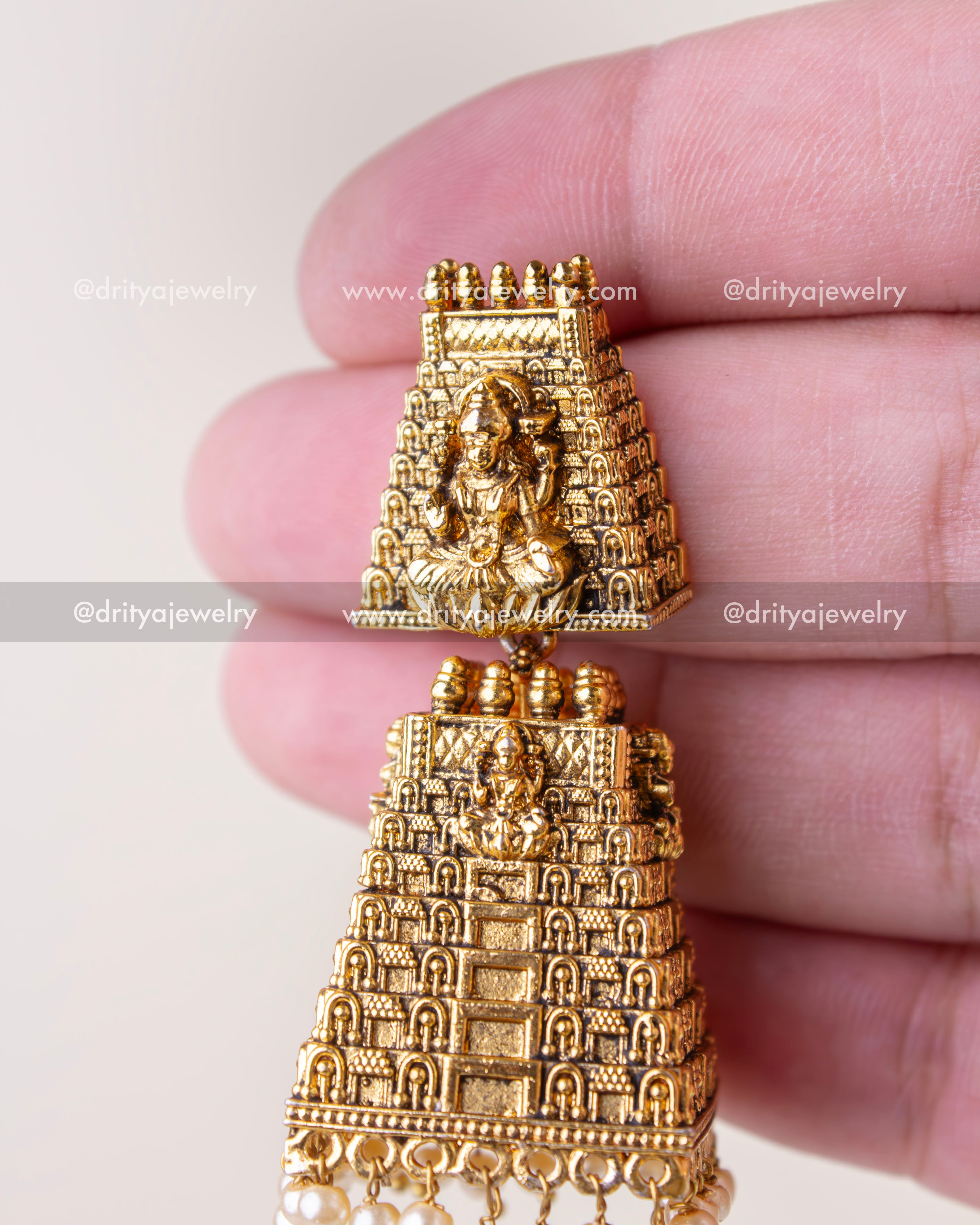 Handheld view of detailed god idol top and gopuram jhumka body in antique gold finish