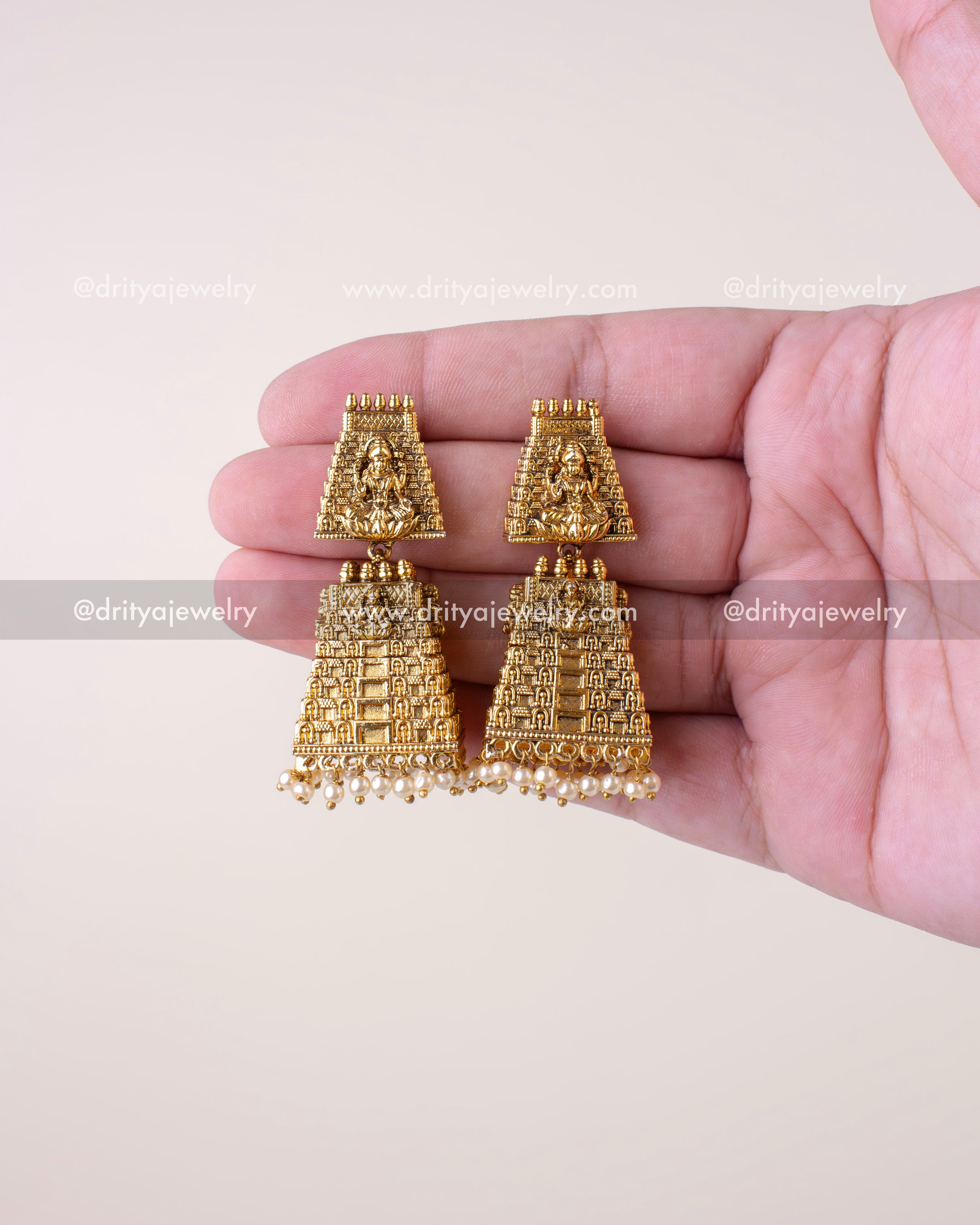 Front view of matching temple god idol jhumka earrings resting on palm
