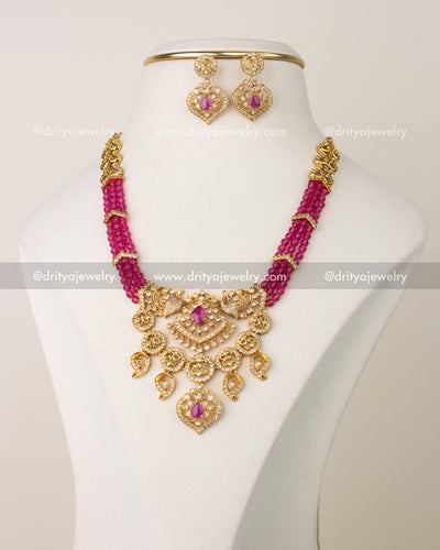 Pink beaded layered necklace set with gold-toned pendant and matching earrings on display bust.