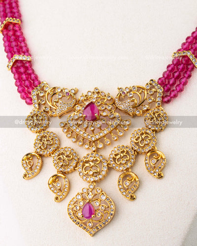 Close-up of ornate gold-toned pendant with pink stones and white stone-studded detailing.