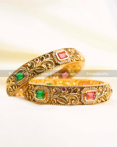 Premium antique gold bangles with floral nakshi engraving and rectangular ruby-pink and green stones.