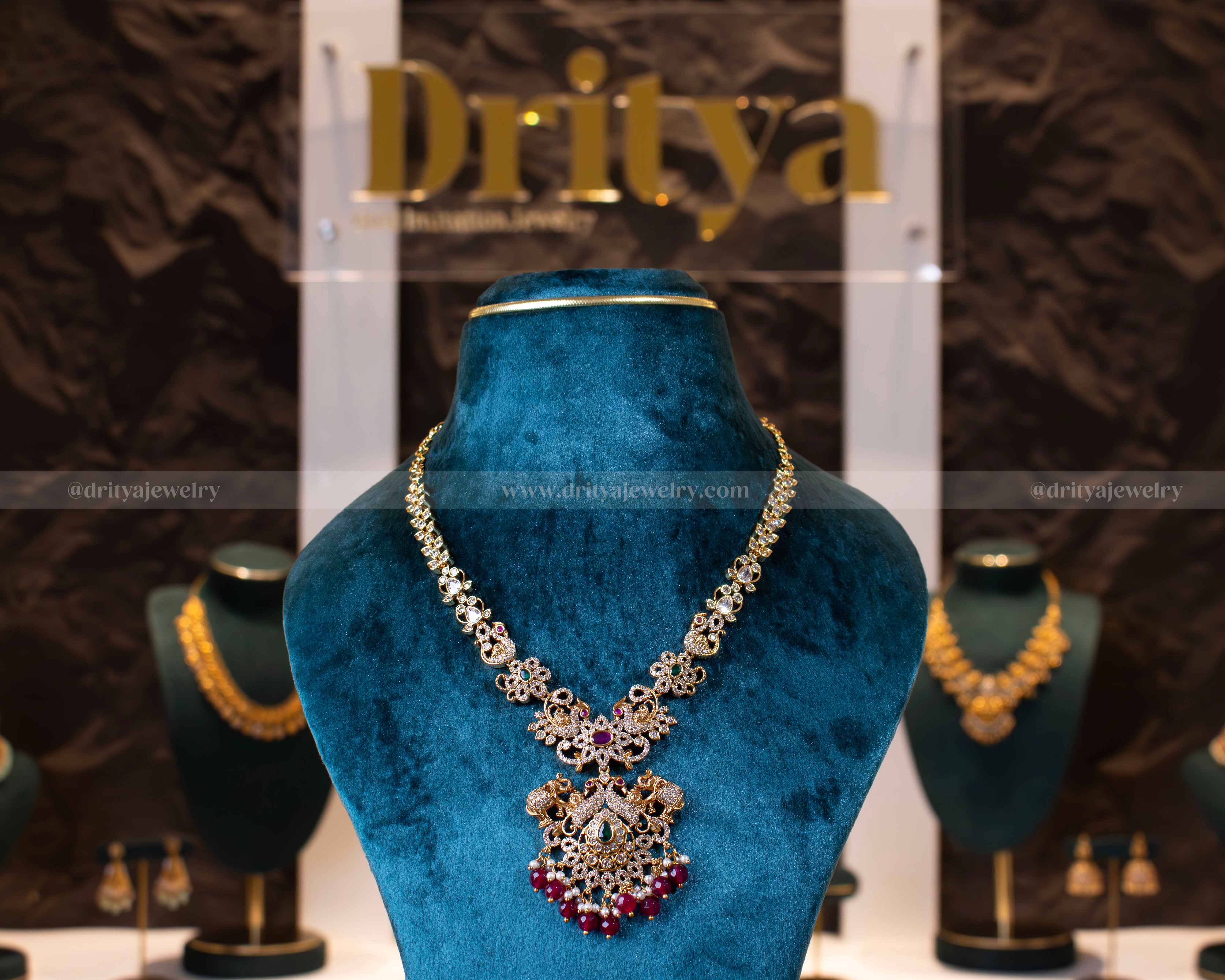 Front view of Dritya Jewelry's antique gold finish necklace set with elephant and peacock motifs, embellished with red beads and pearls.