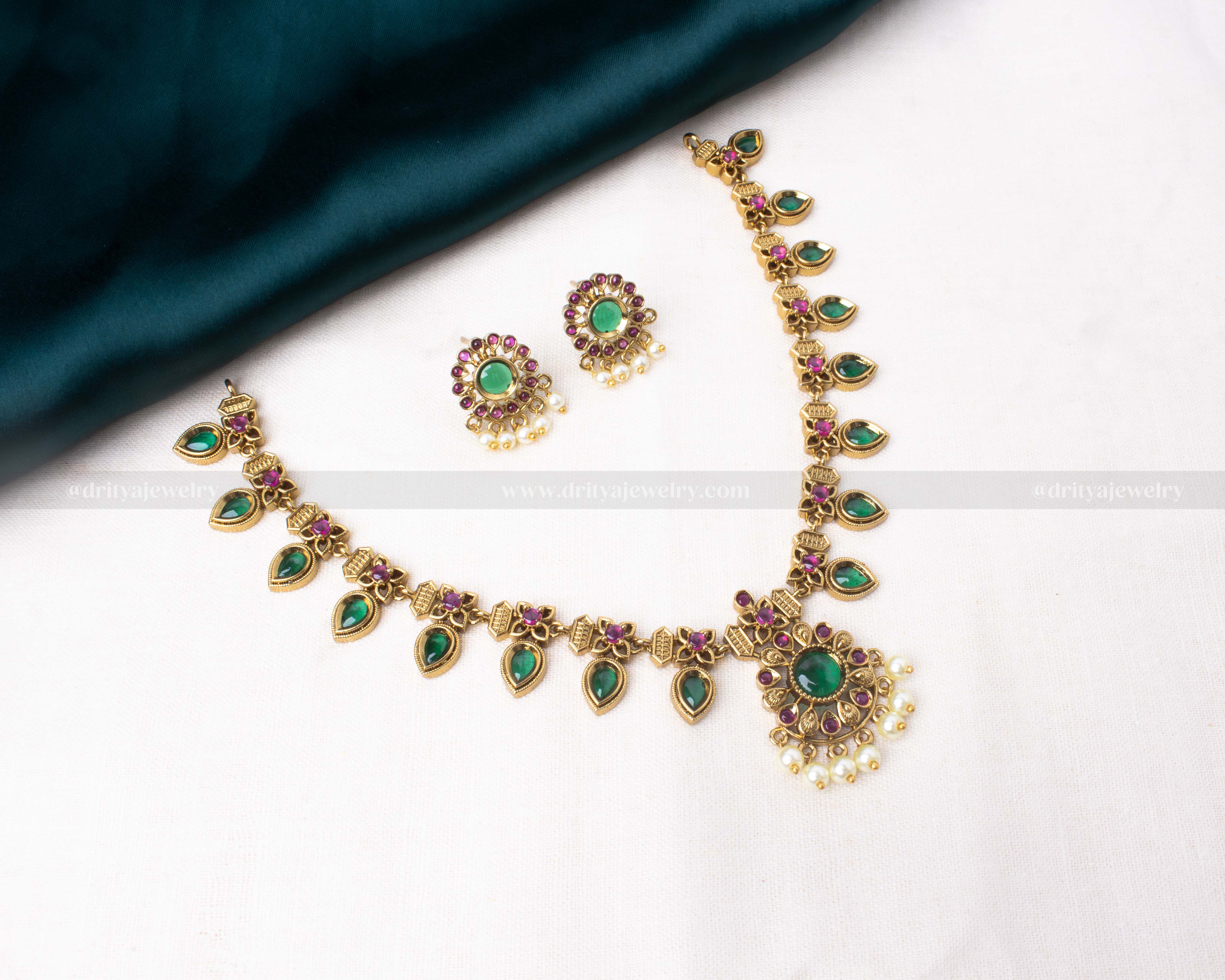 Jadau-inspired antique gold necklace set with green and ruby-like stones, pearls, and matching earrings.