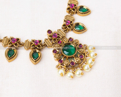 Jadau-inspired antique gold necklace set with green and ruby-like stones, pearls, and matching earrings.