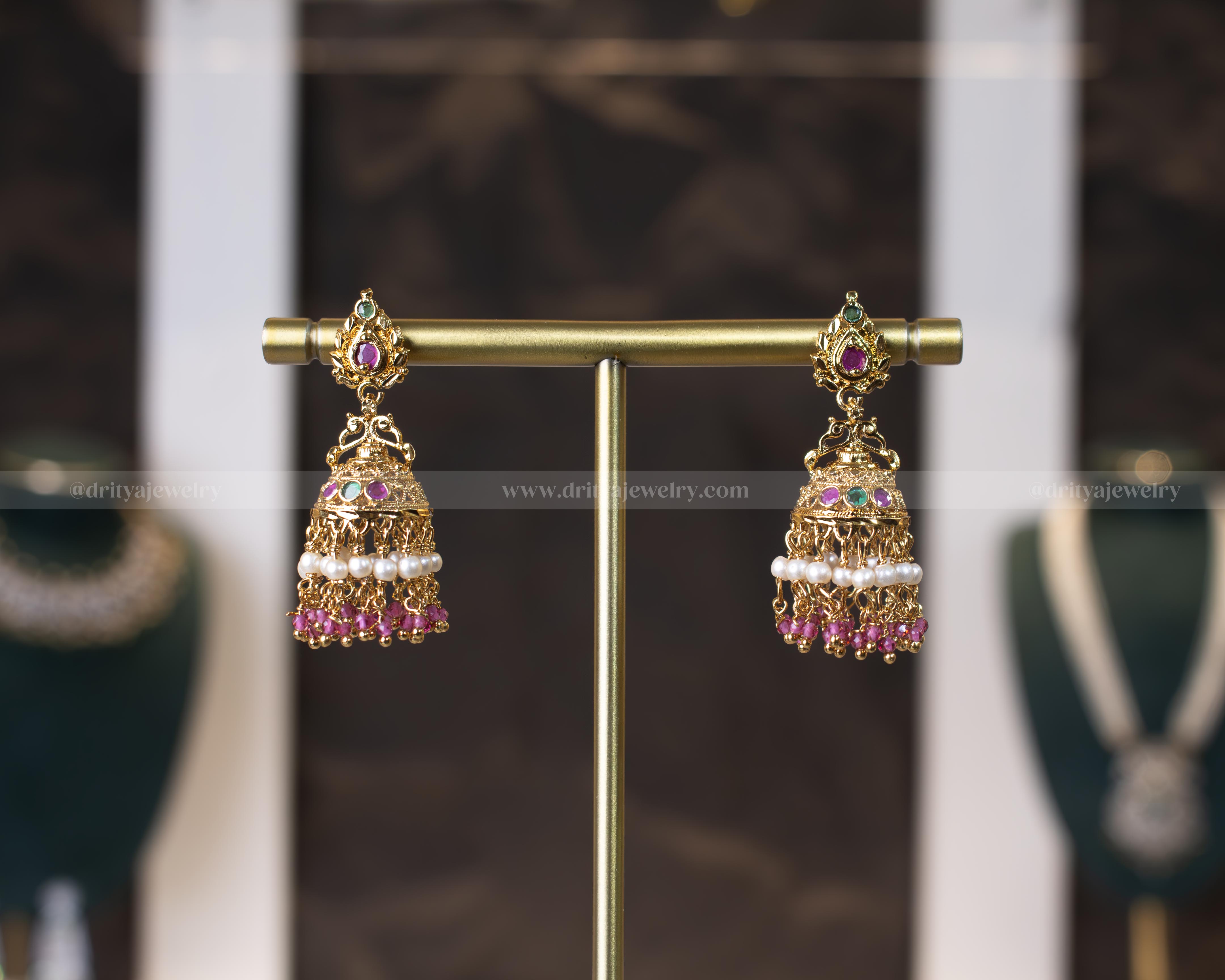 Elegant antique gold-polished jhumka earrings with ruby and emerald gemstones and pearl danglers by Dritya Jewelry.