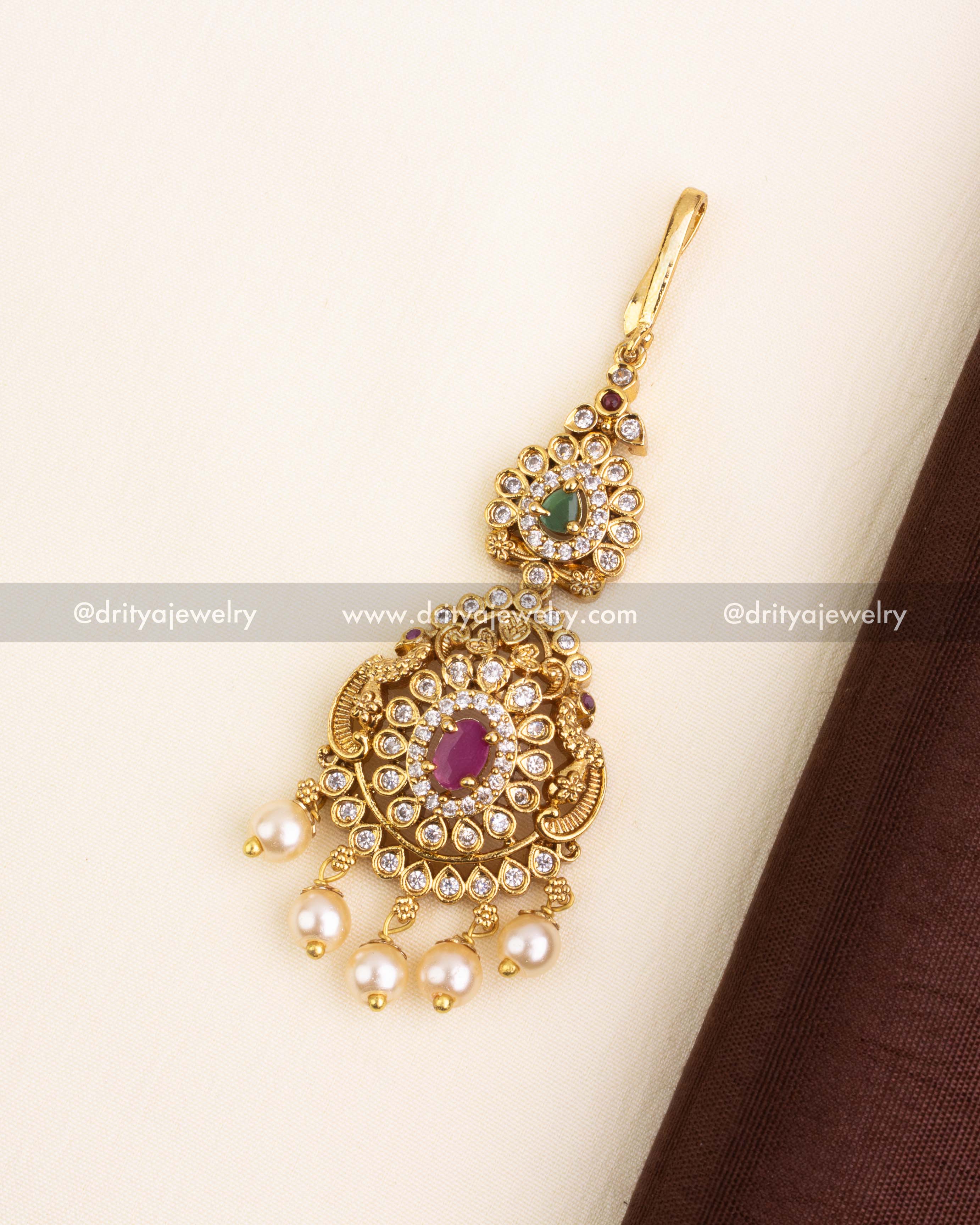 Traditional gold-finish maang tikka with CZ stones, ruby and green accents, and pearl danglers.
