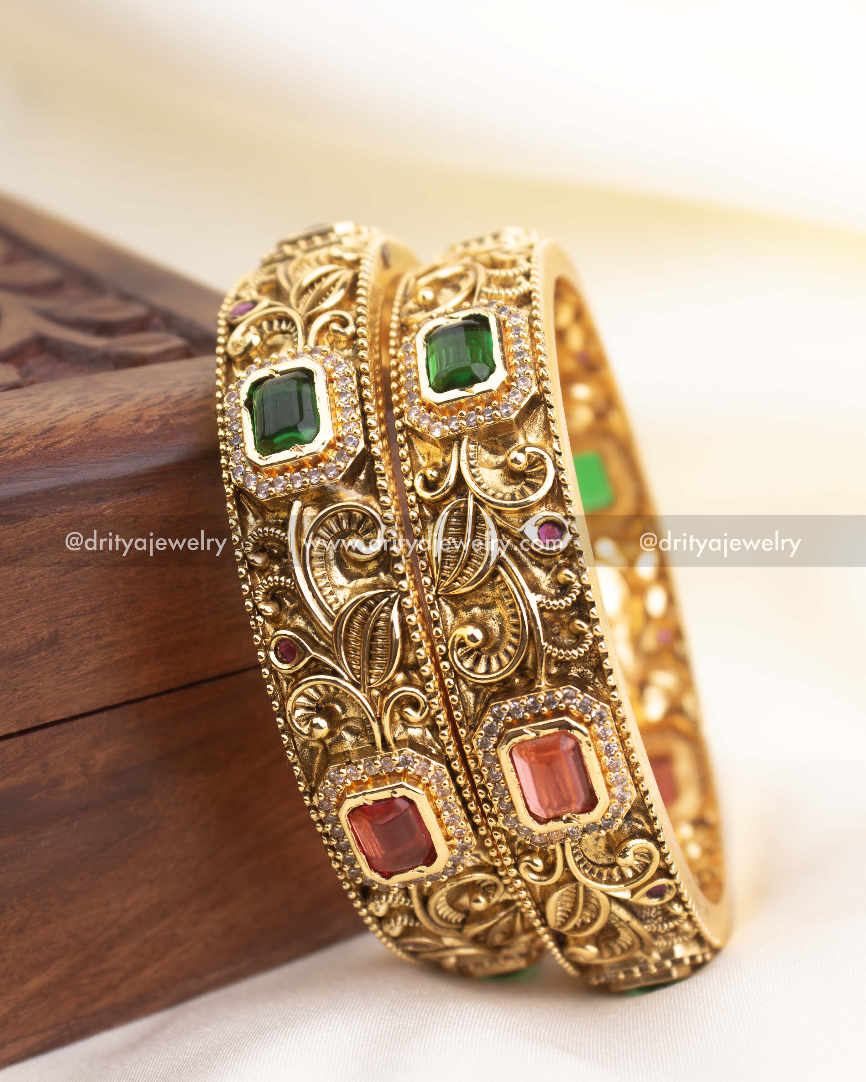 Detailed side profile of antique gold bangles showcasing floral carvings and rectangular stone placements.