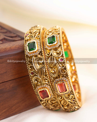 Detailed side profile of antique gold bangles showcasing floral carvings and rectangular stone placements.