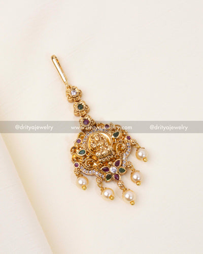 Regal Nakshi Maang Tikka featuring a Lakshmi motif, adorned with CZ stones, ruby, emerald accents, and pearl embellishments.