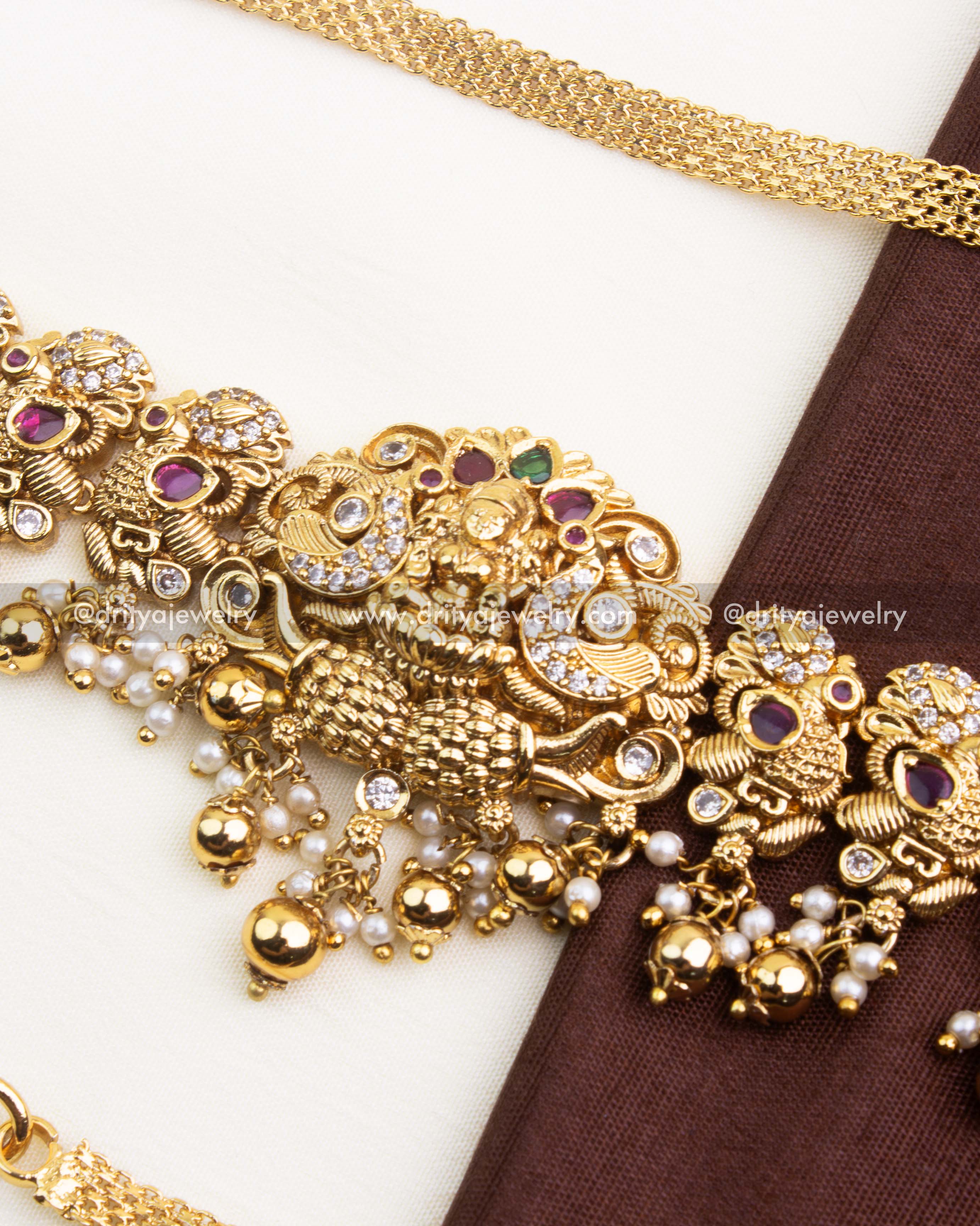 Close up of central motif on Nakshi hip chain with intricate carving, ruby red stones, and hanging pearl drops.