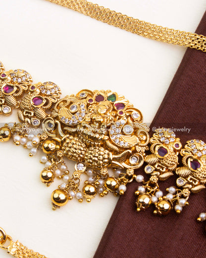 Close up of central motif on Nakshi hip chain with intricate carving, ruby red stones, and hanging pearl drops.