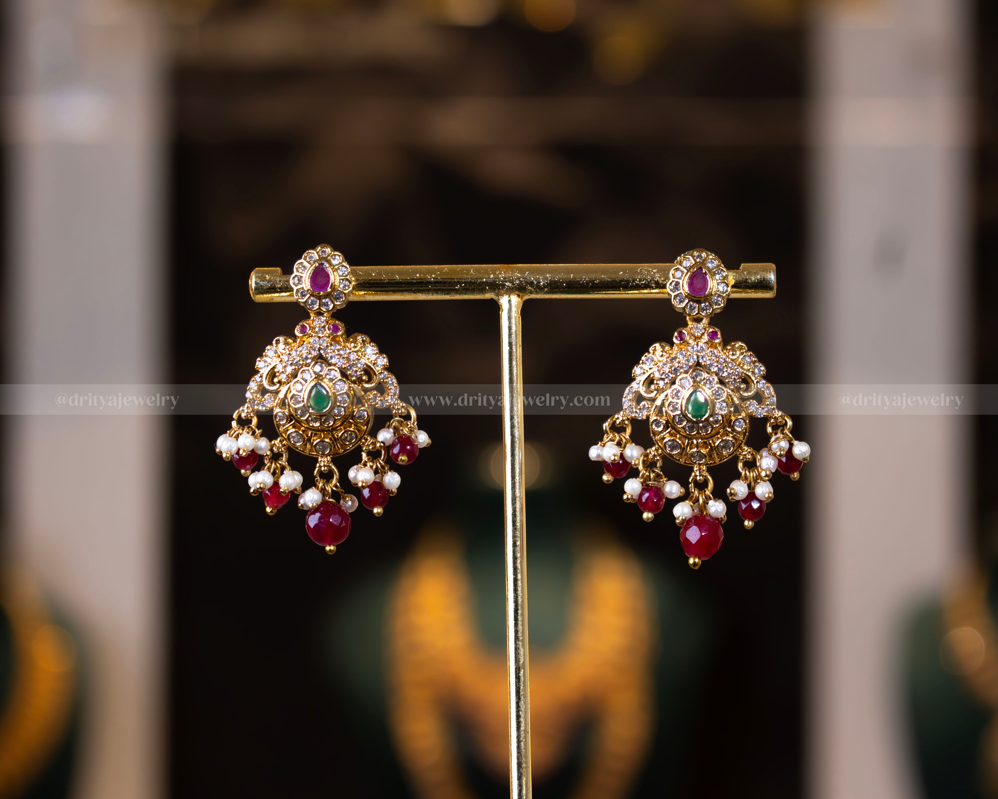 Front view of matching chandbali earrings from Dritya Jewelry's antique gold finish necklace set, adorned with red beads and sparkling stones.