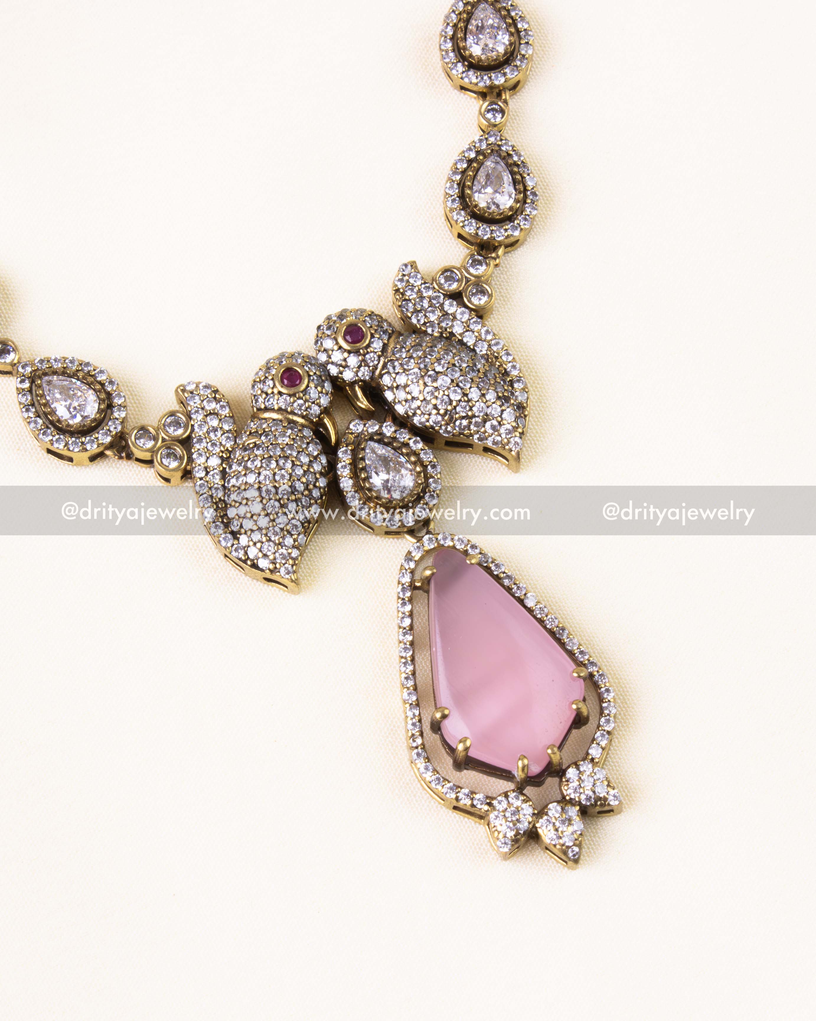 Close-up of the parrot motif encrusted with CZ stones and a teardrop-shaped pink stone pendant.